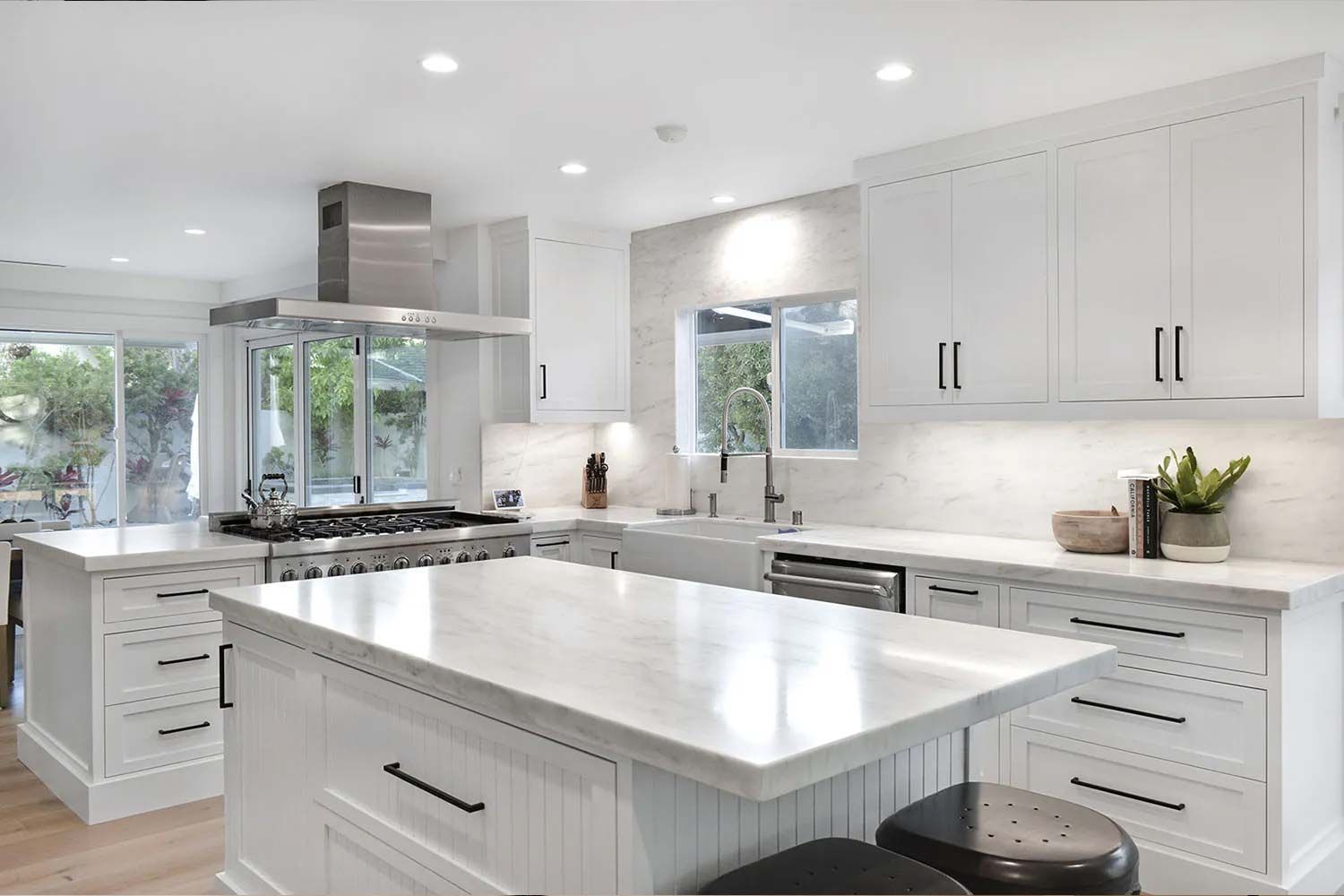 White modern kitchen with marble countertops, stainless steel appliances, and an island.