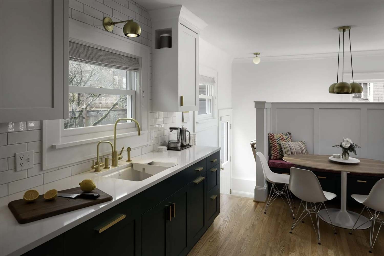 Modern kitchen with dark green cabinets, gold fixtures, and a small round table with white chairs.