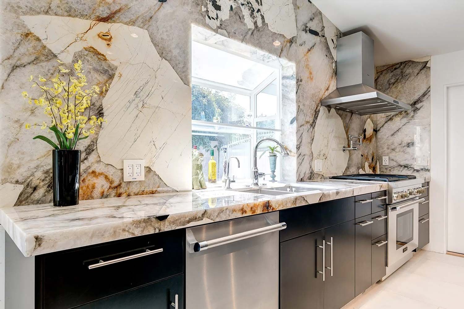 Kitchen with marble countertops and backsplash, black cabinets, stainless steel appliances, and a window.