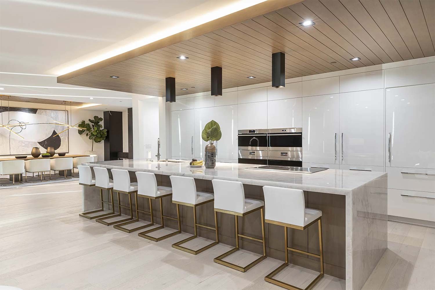 Luxurious modern kitchen with white cabinets, marble island, gold stools, and wood ceiling.