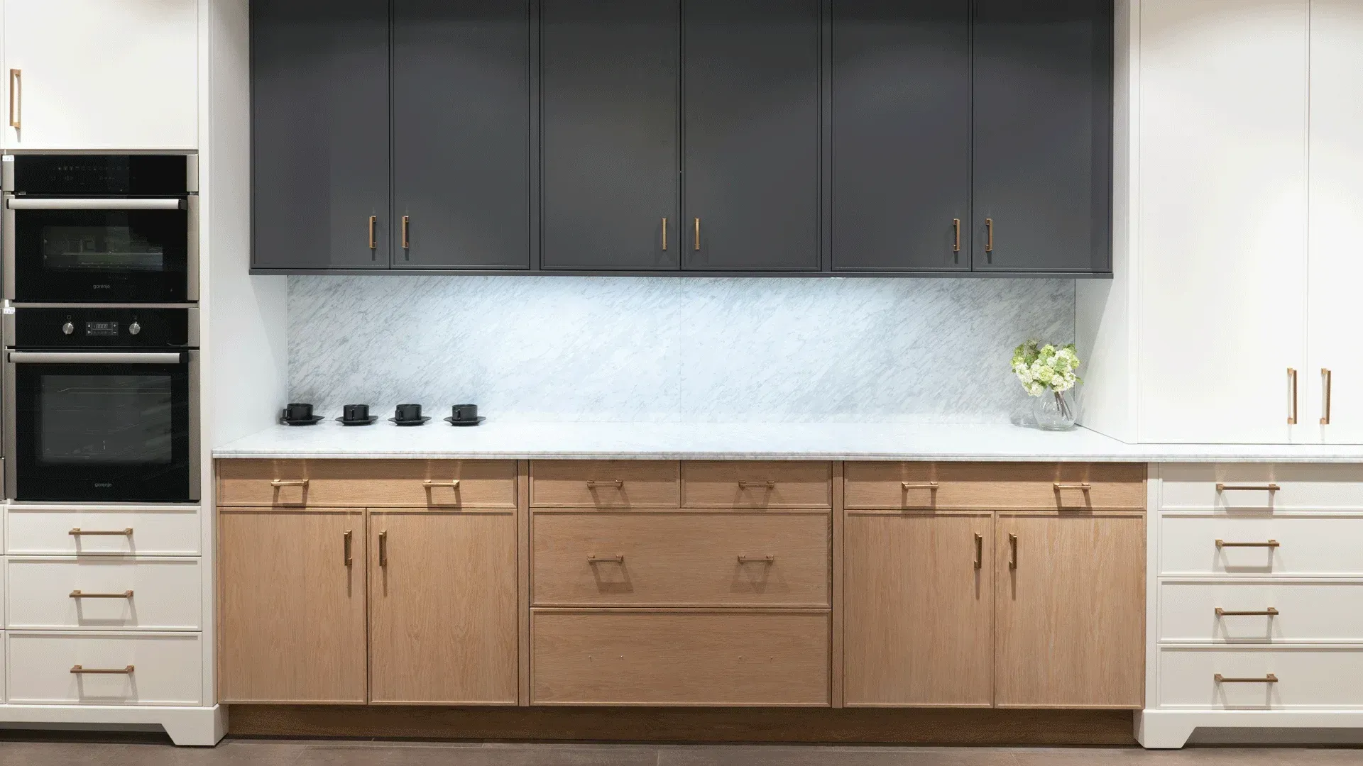 Modern kitchen with white and wood cabinets, gray uppers, and a marble backsplash.