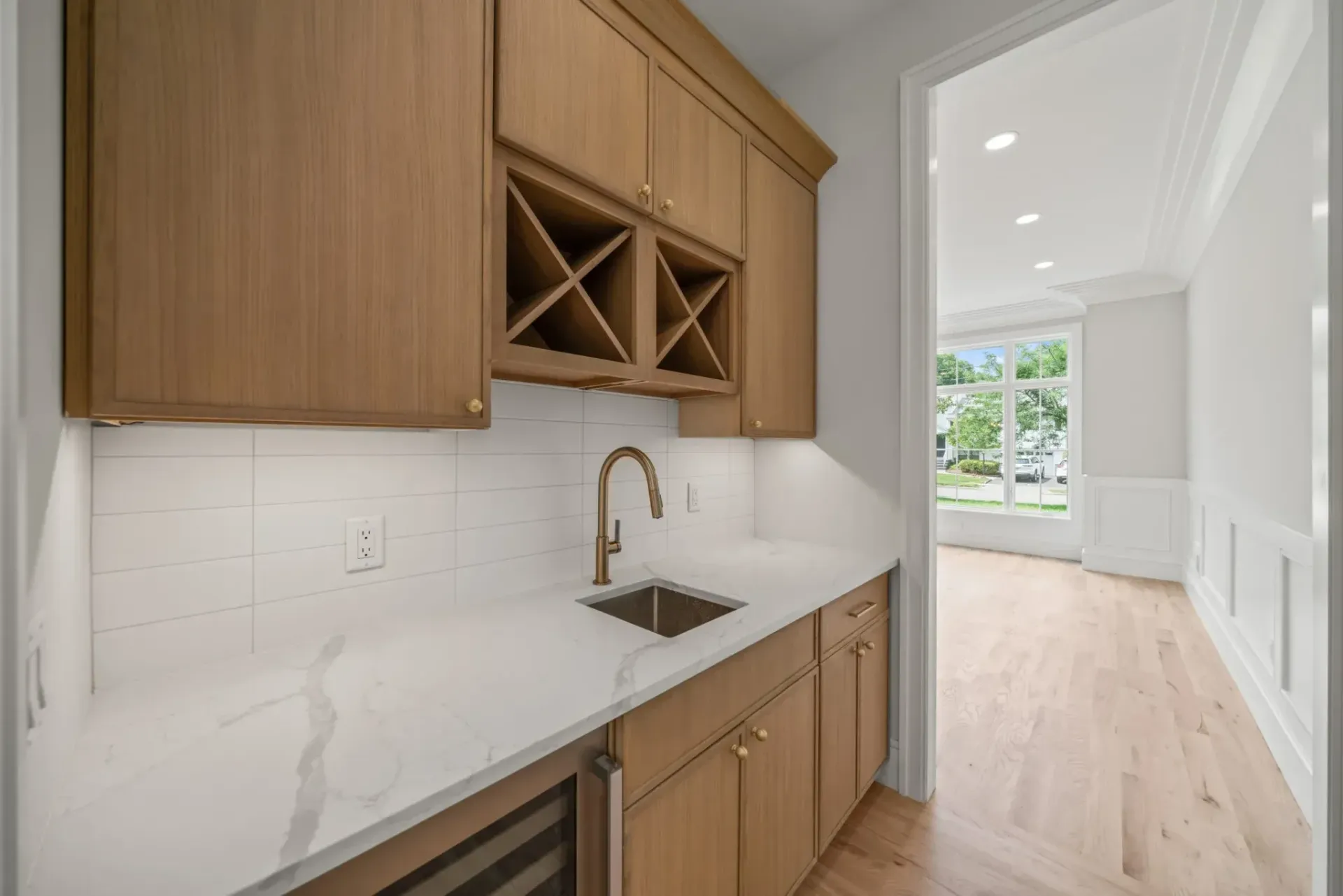 Oak cabinets with wine rack and sink in a bar area, light wood floors, and access to another room.