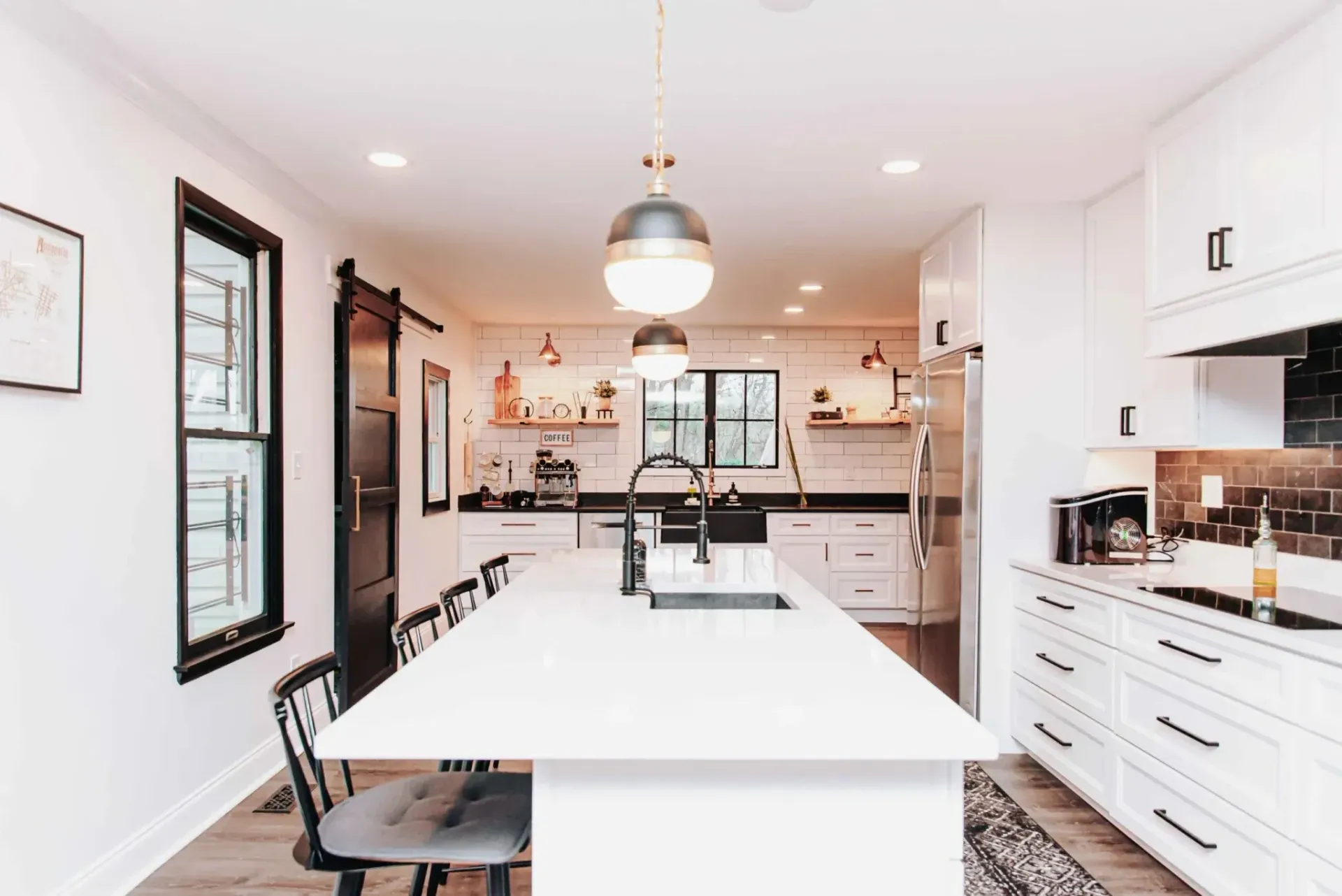 Modern kitchen with white cabinets, island, and black accents; gold light fixtures.