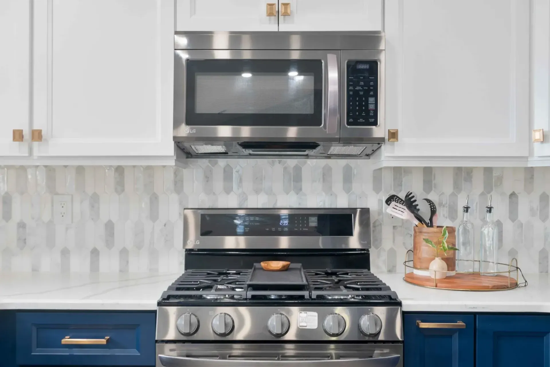 Stainless steel stove and microwave with white and blue cabinets in a kitchen.