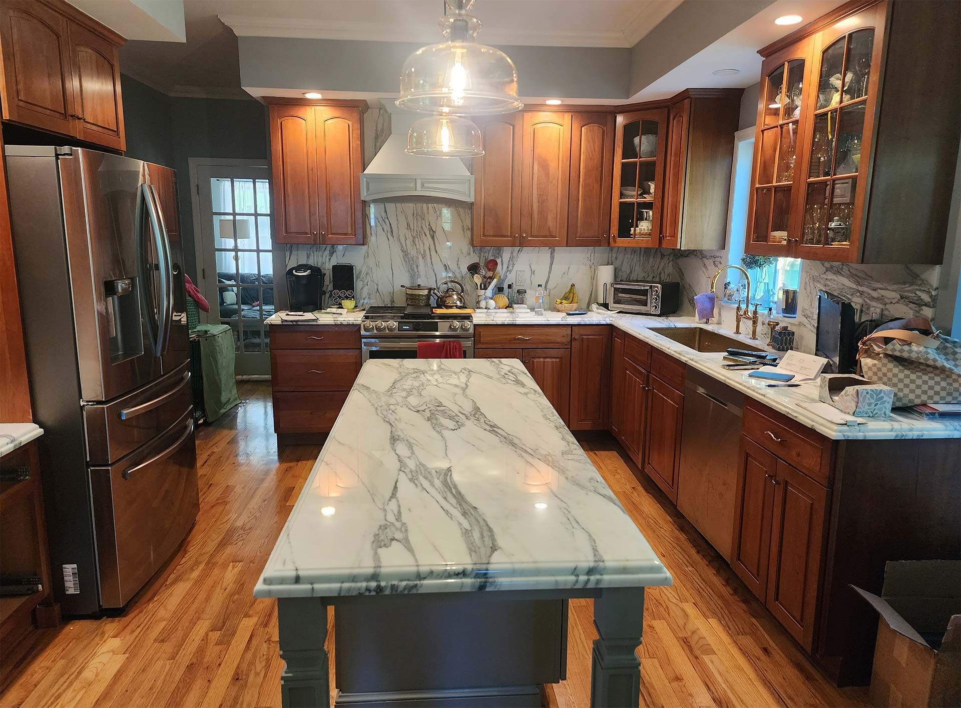 Kitchen with wood cabinets, white marble island, stainless steel appliances, and light fixtures.