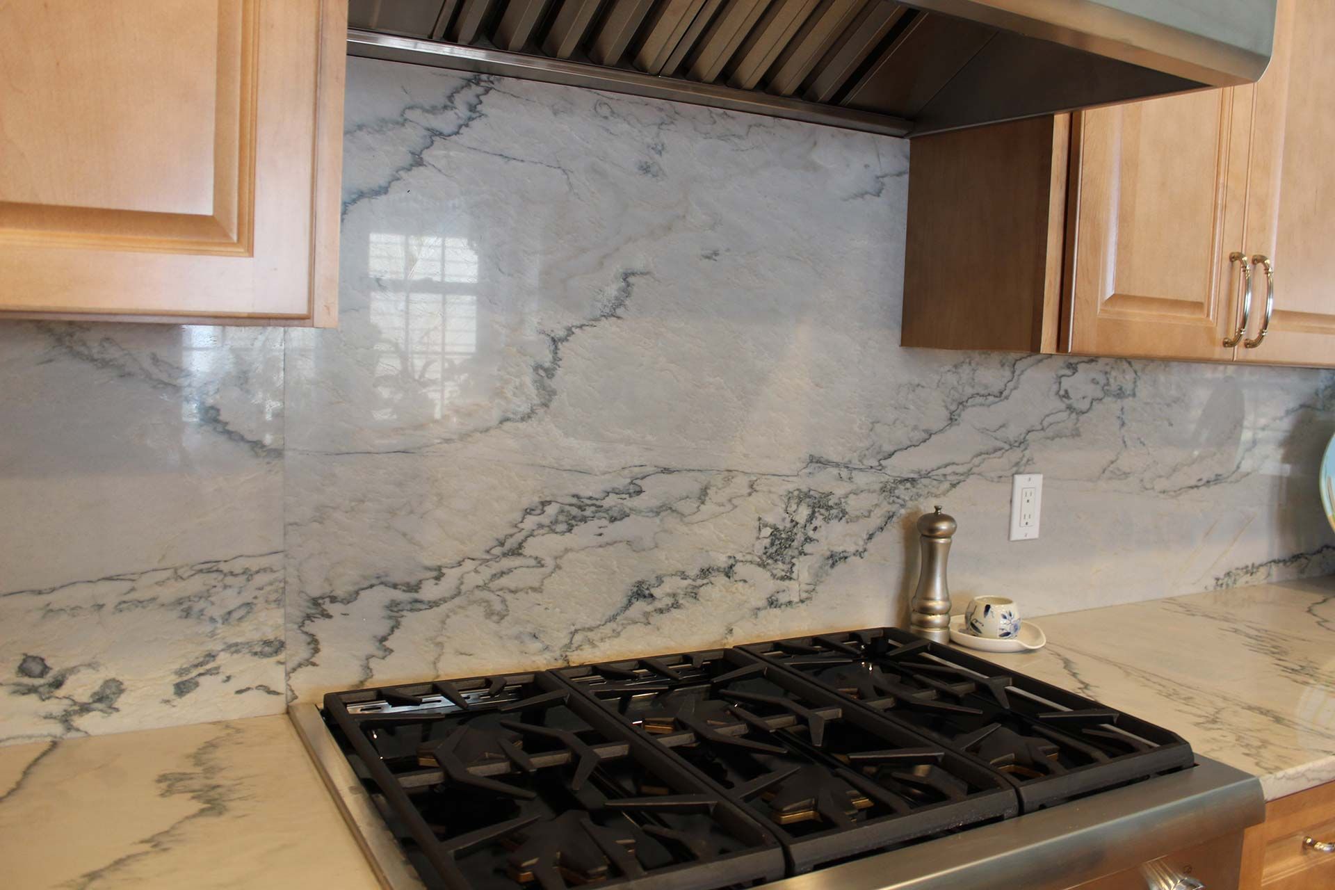 Kitchen with gas stovetop, marble backsplash, light cabinets.