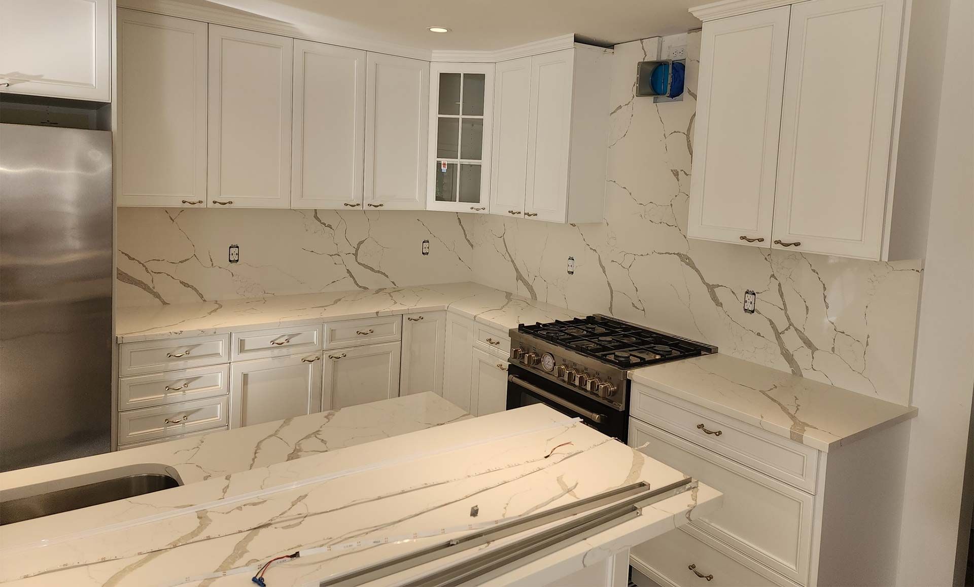 White kitchen with marble-look countertops, stainless steel appliances, and a gas range.
