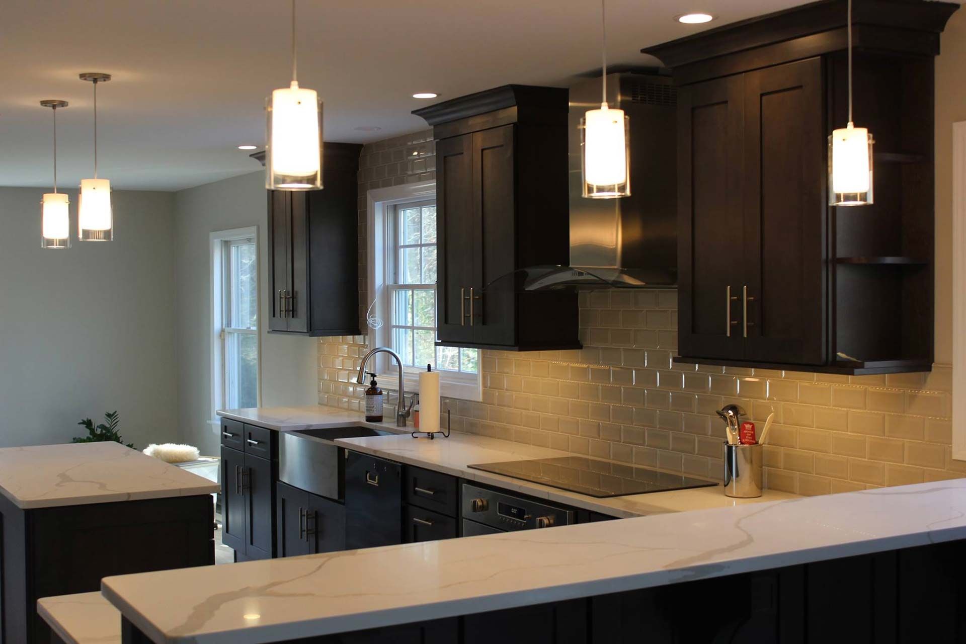 Dark kitchen with white countertops, pendant lights, stainless steel appliances, and dark cabinets.