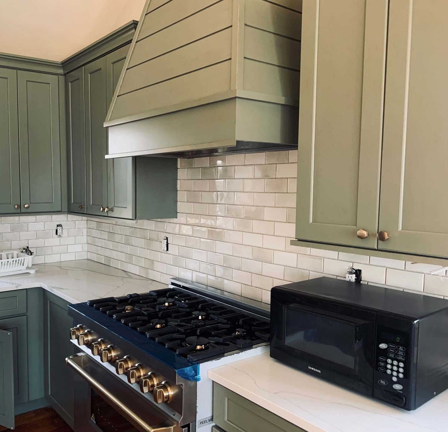 Green kitchen cabinets, range hood, white subway tile backsplash, range, and microwave.