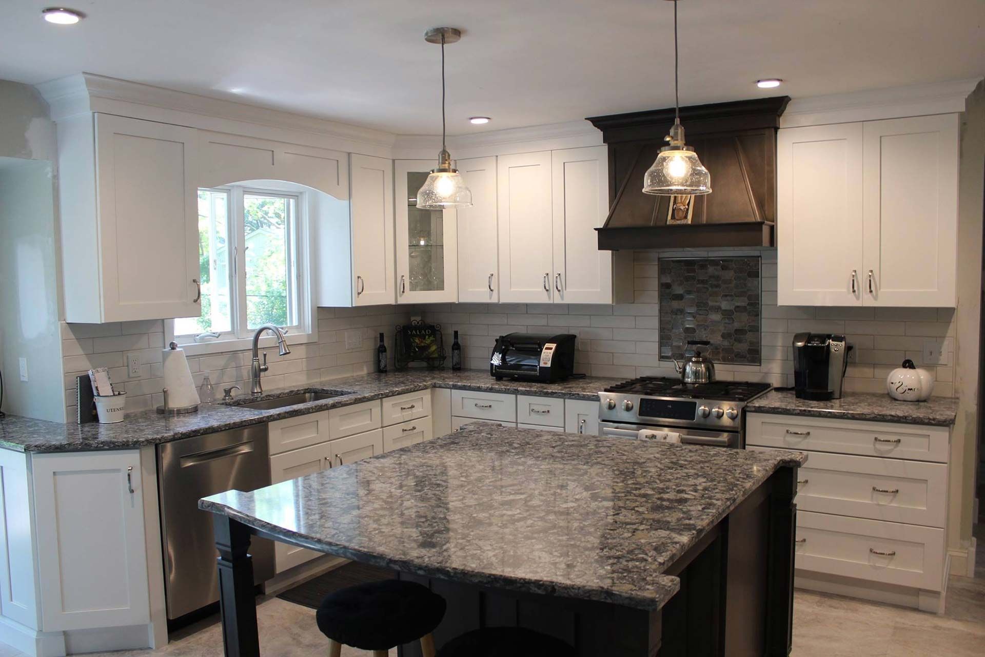 White kitchen with dark granite counters, island, and cabinets; stove hood.