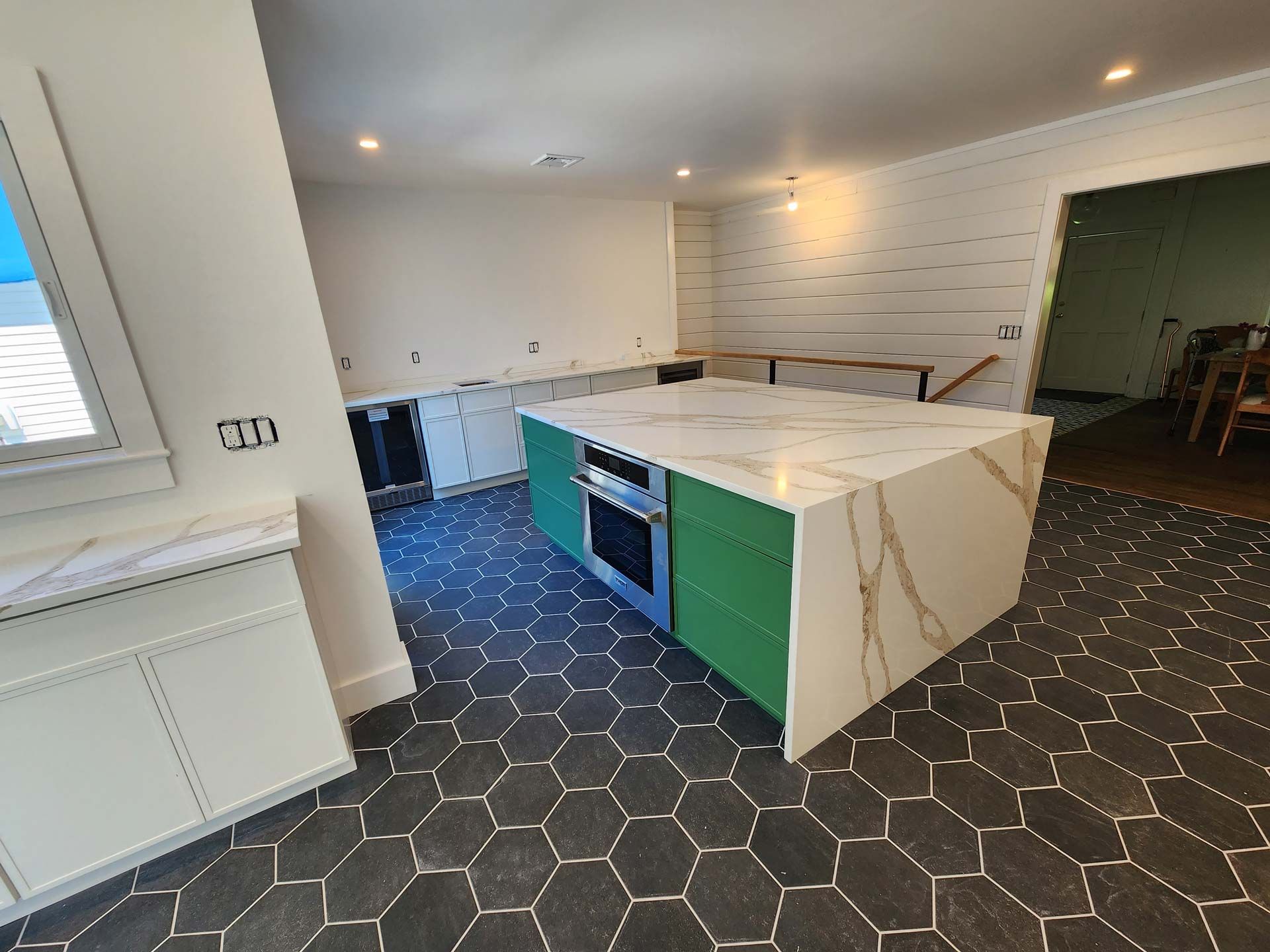 Kitchen remodel with green island, white countertops, dark hexagon tile floor.