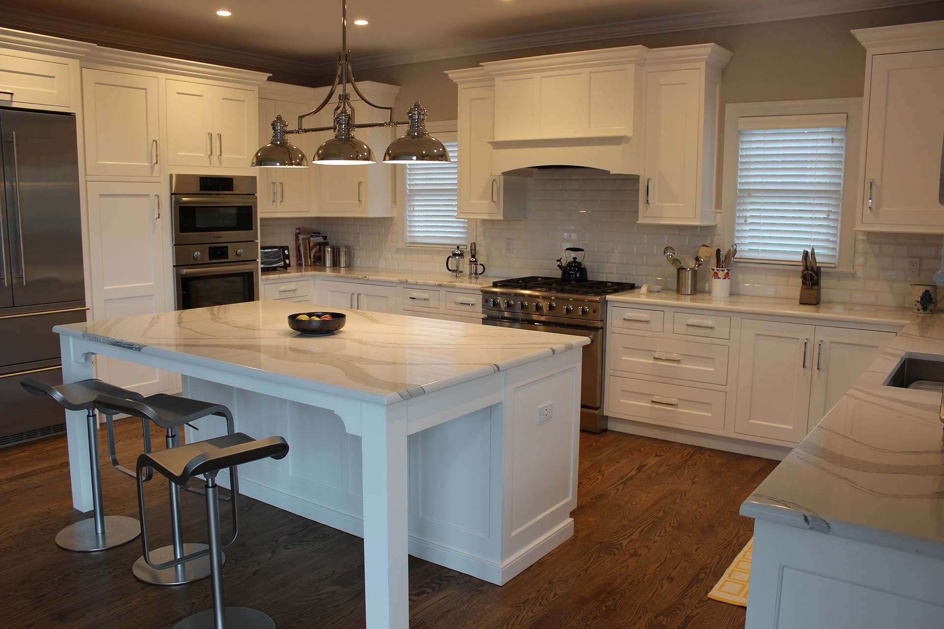 White kitchen with island, stainless steel appliances, and wood floors.