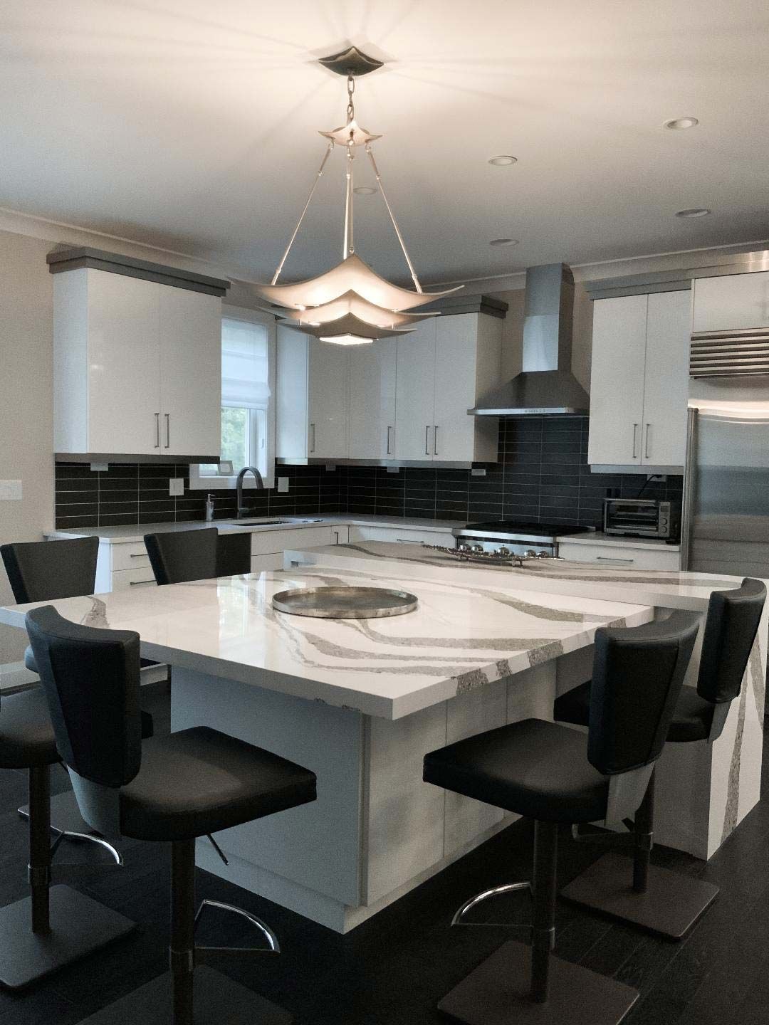 Modern kitchen with large island, white cabinets, black countertops, and black leather bar stools.