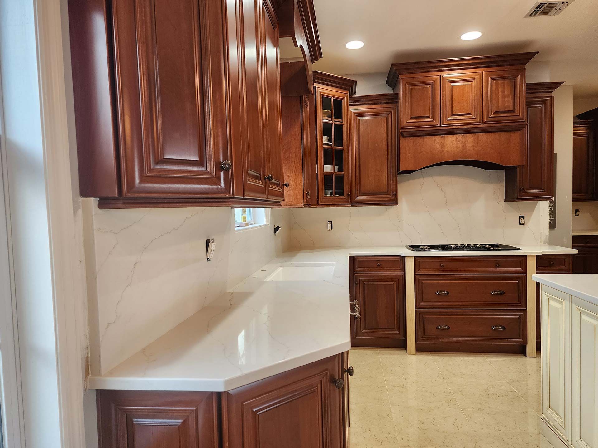 A kitchen with dark brown cabinets, white countertops, and a light-colored backsplash.
