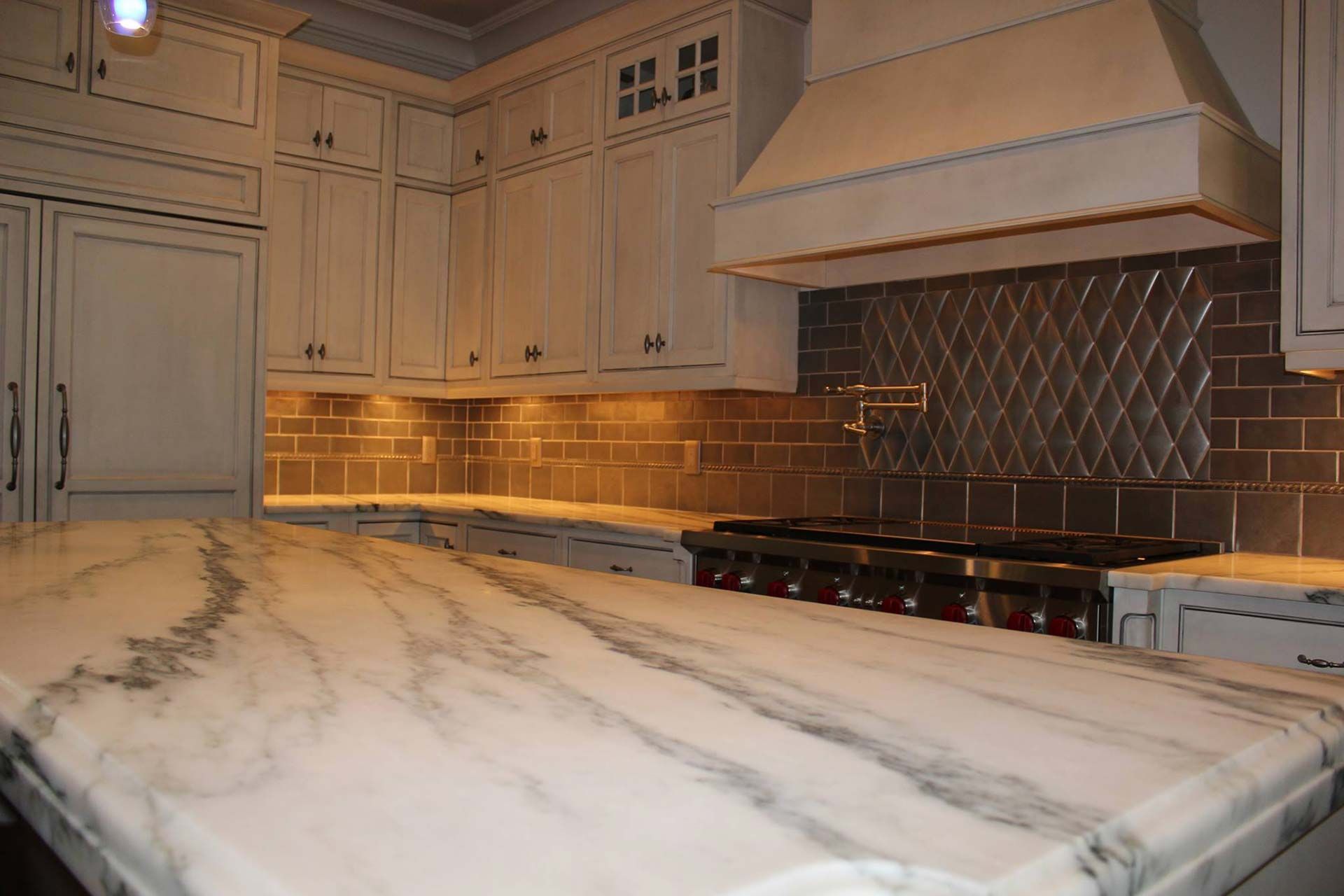 Kitchen with white marble countertop, light cabinets, metal backsplash, and range.