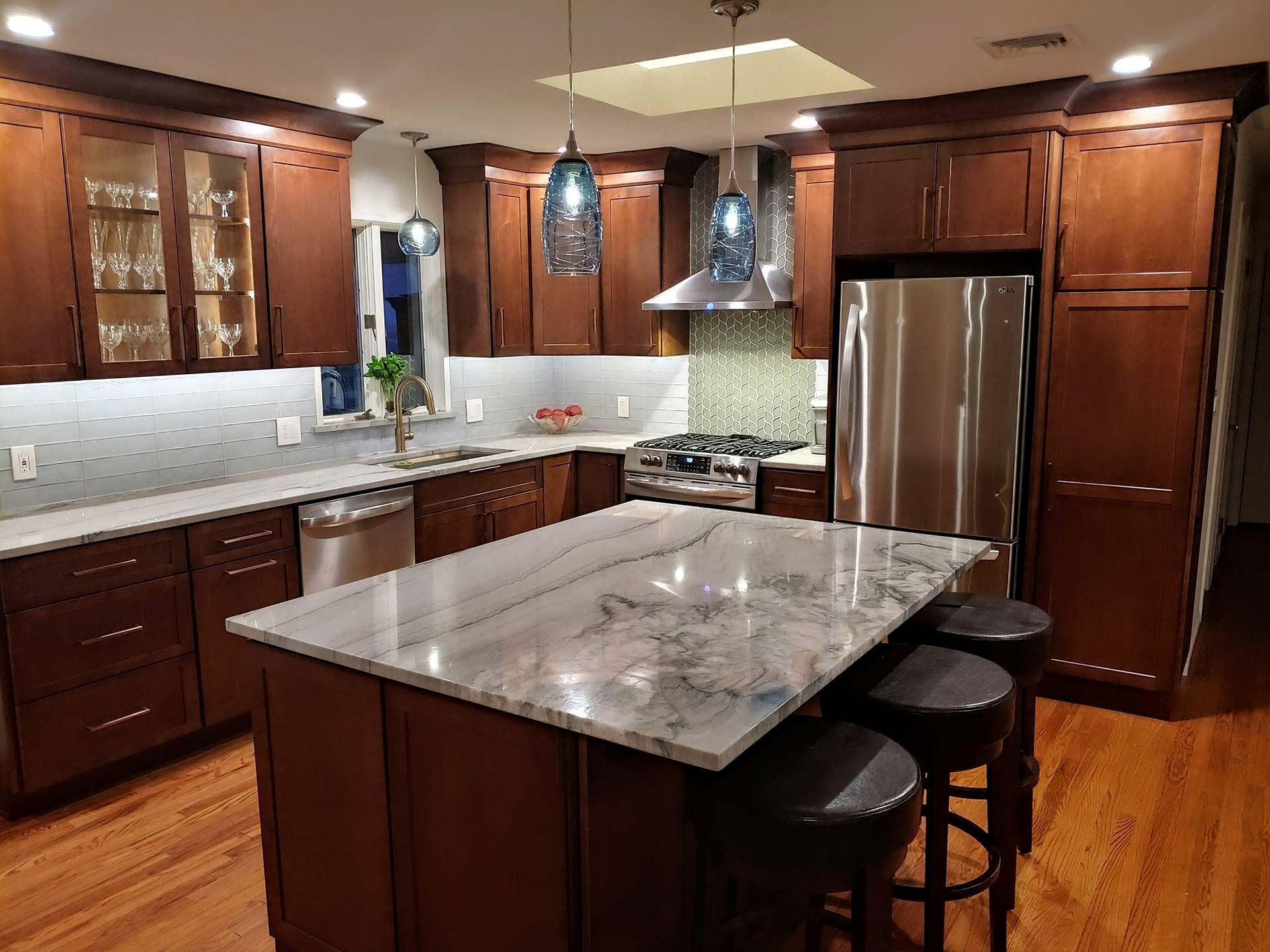 Modern kitchen with dark wood cabinets, stainless steel appliances, and a marble island.