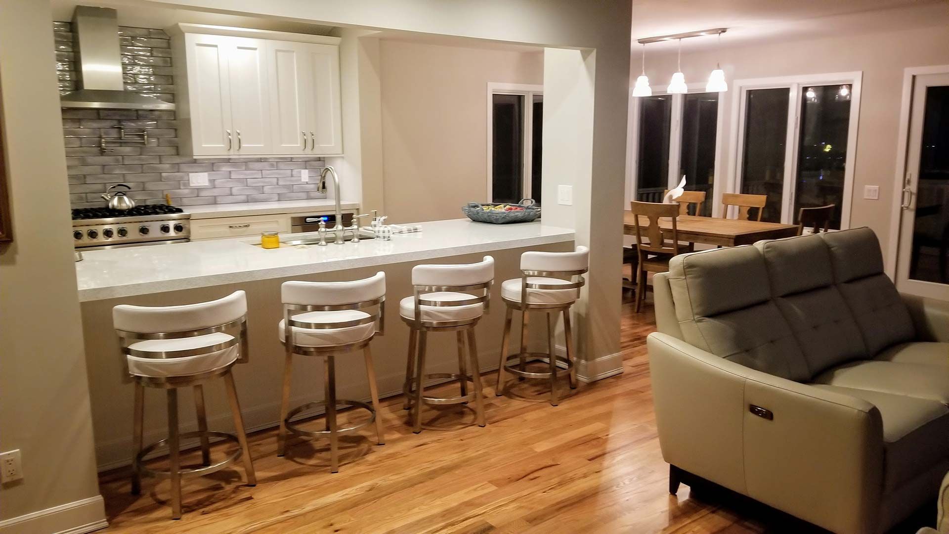 Kitchen with white cabinets, bar stools, and open to a dining and living area with wood floors.