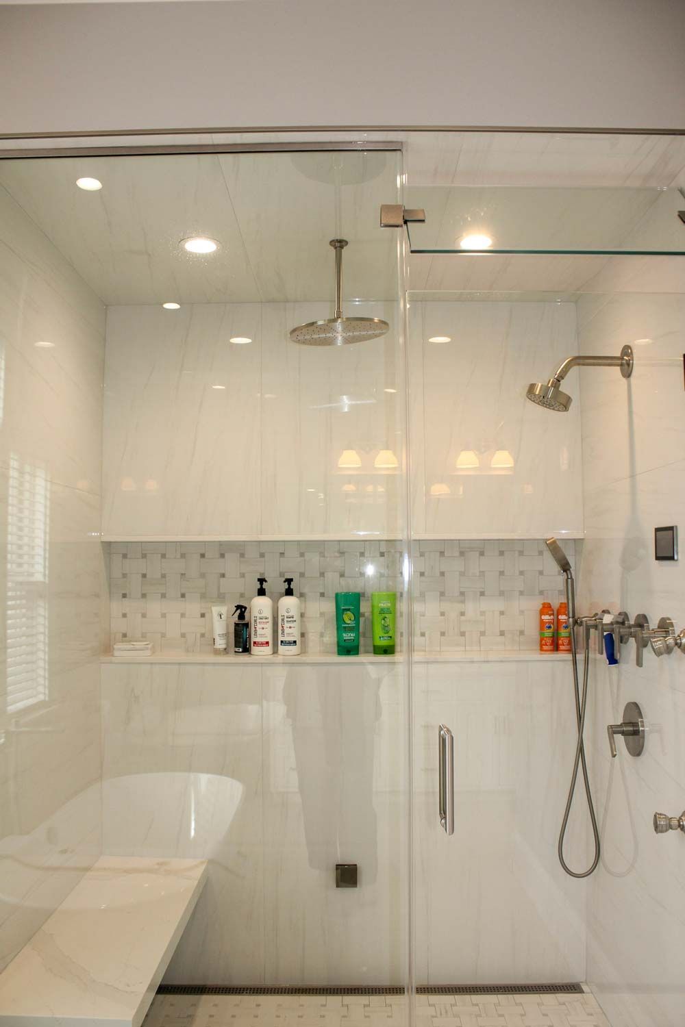 A modern, white tiled shower with glass door, built-in bench, and multiple showerheads.