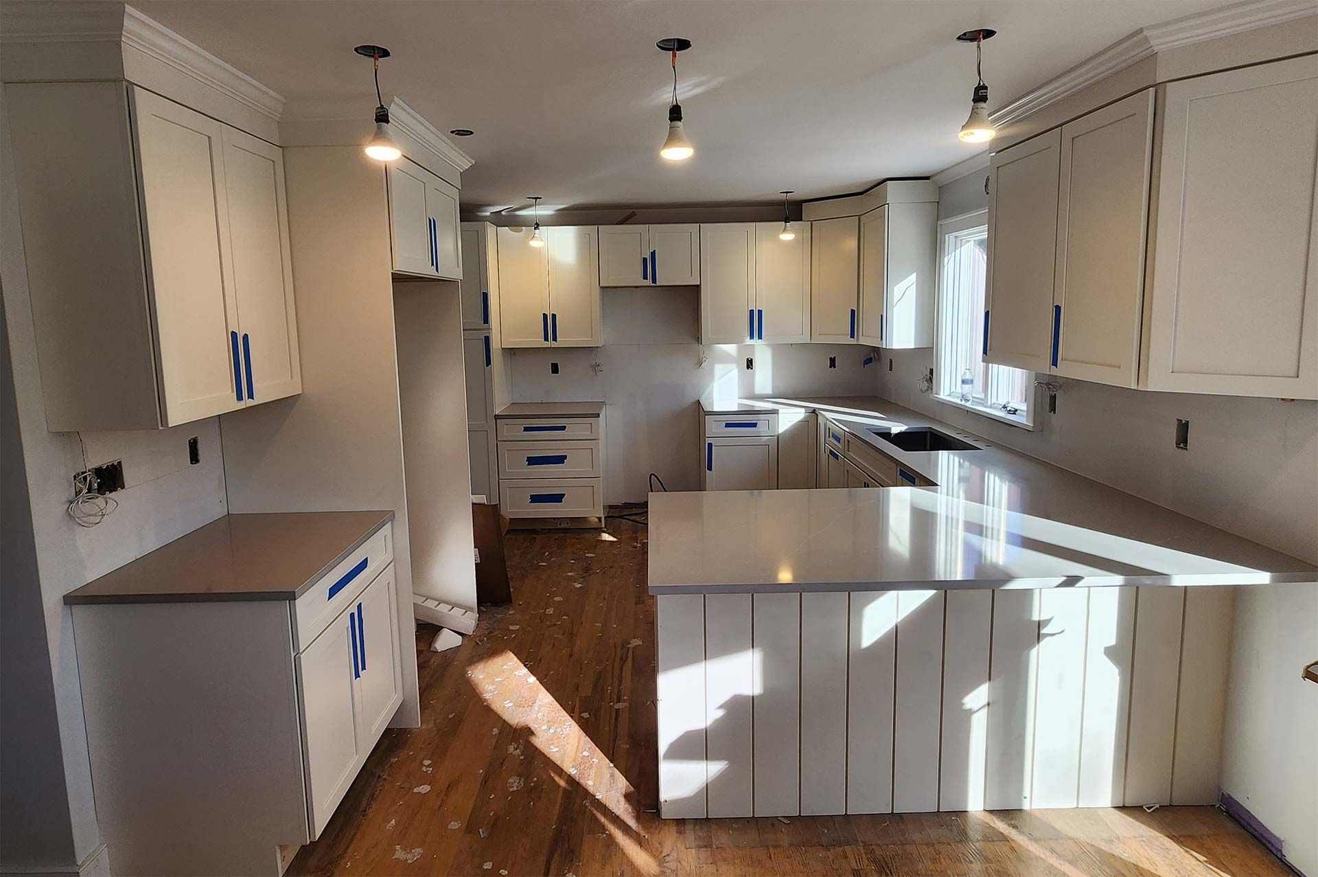 A white kitchen under renovation, cabinets installed, island with countertop, new hardwood floors.