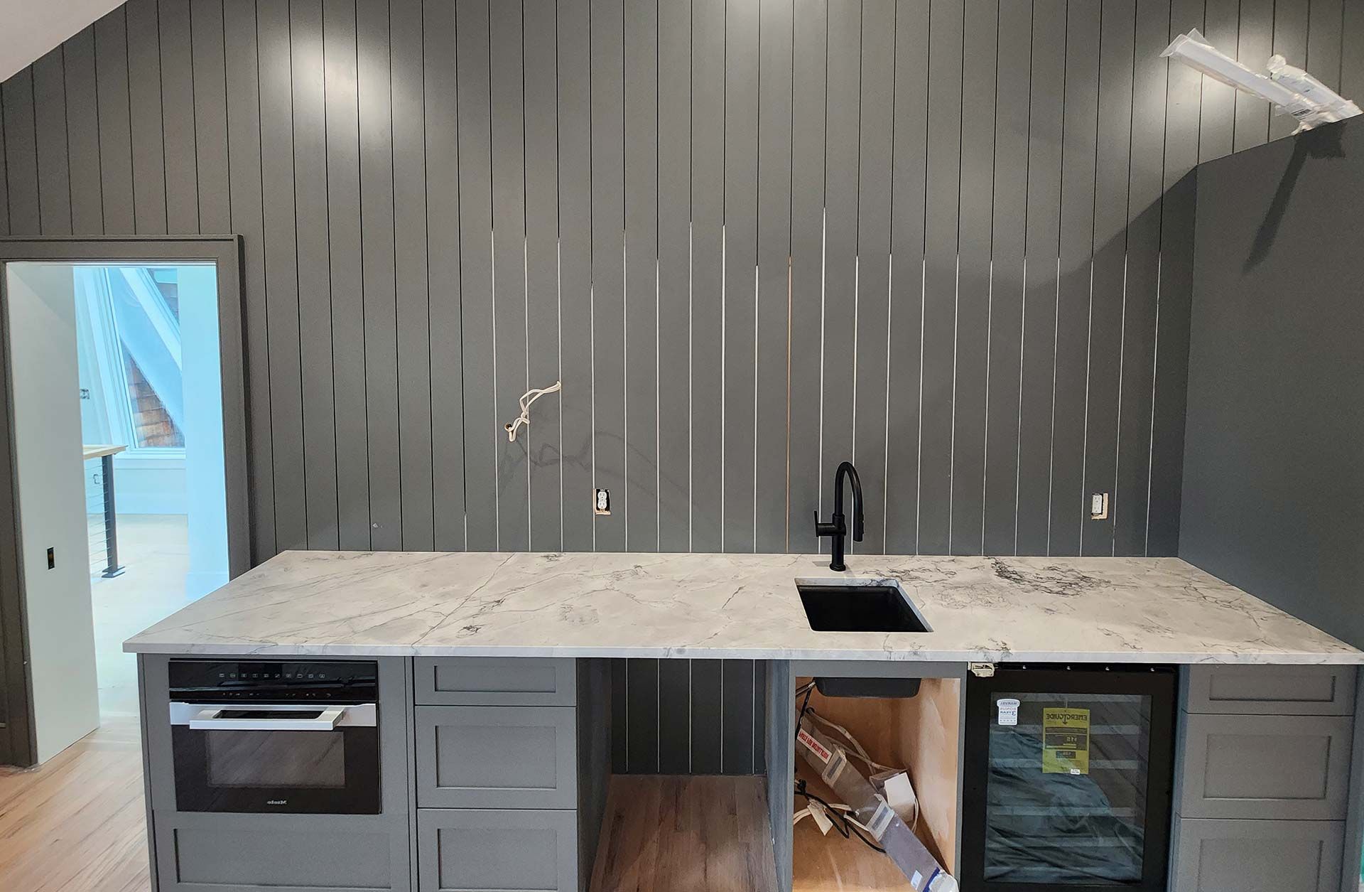 Modern kitchen with gray cabinets, marble countertop, black faucet, and vertically striped gray wall.