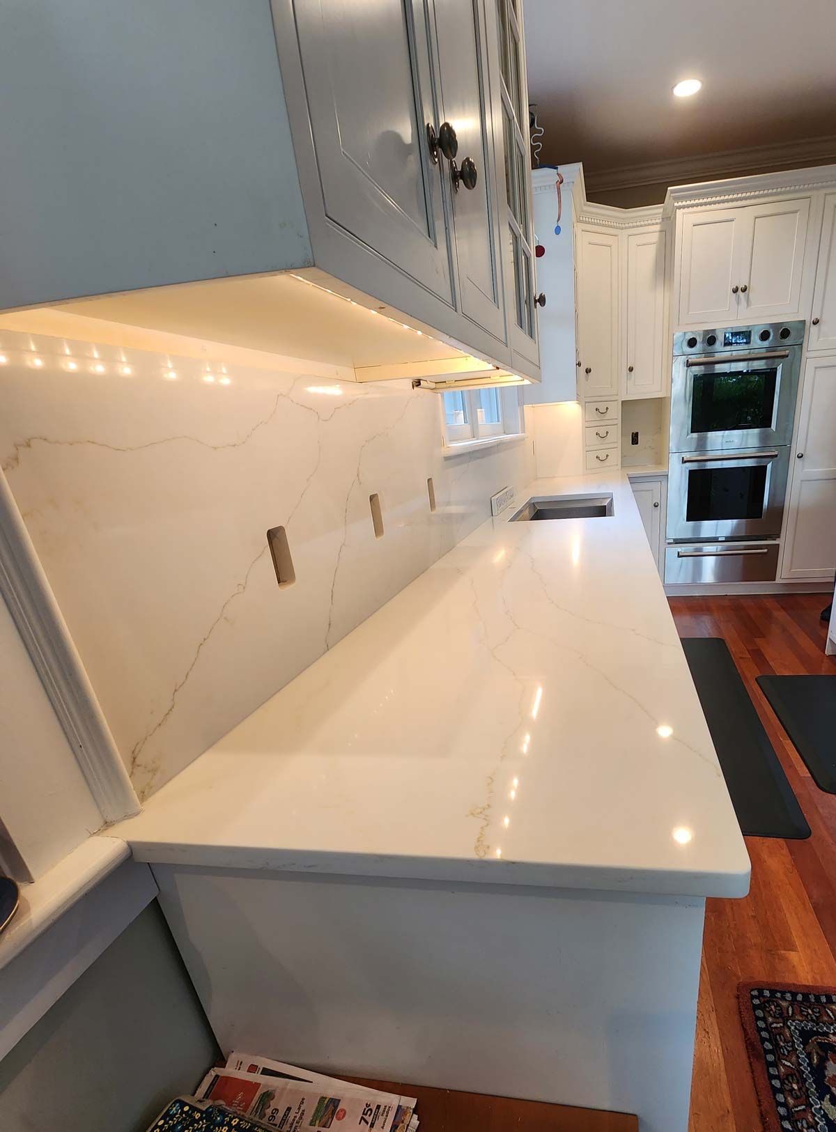 Kitchen with white countertops, cabinets, and backsplash. Overhead lighting and stainless steel appliances.