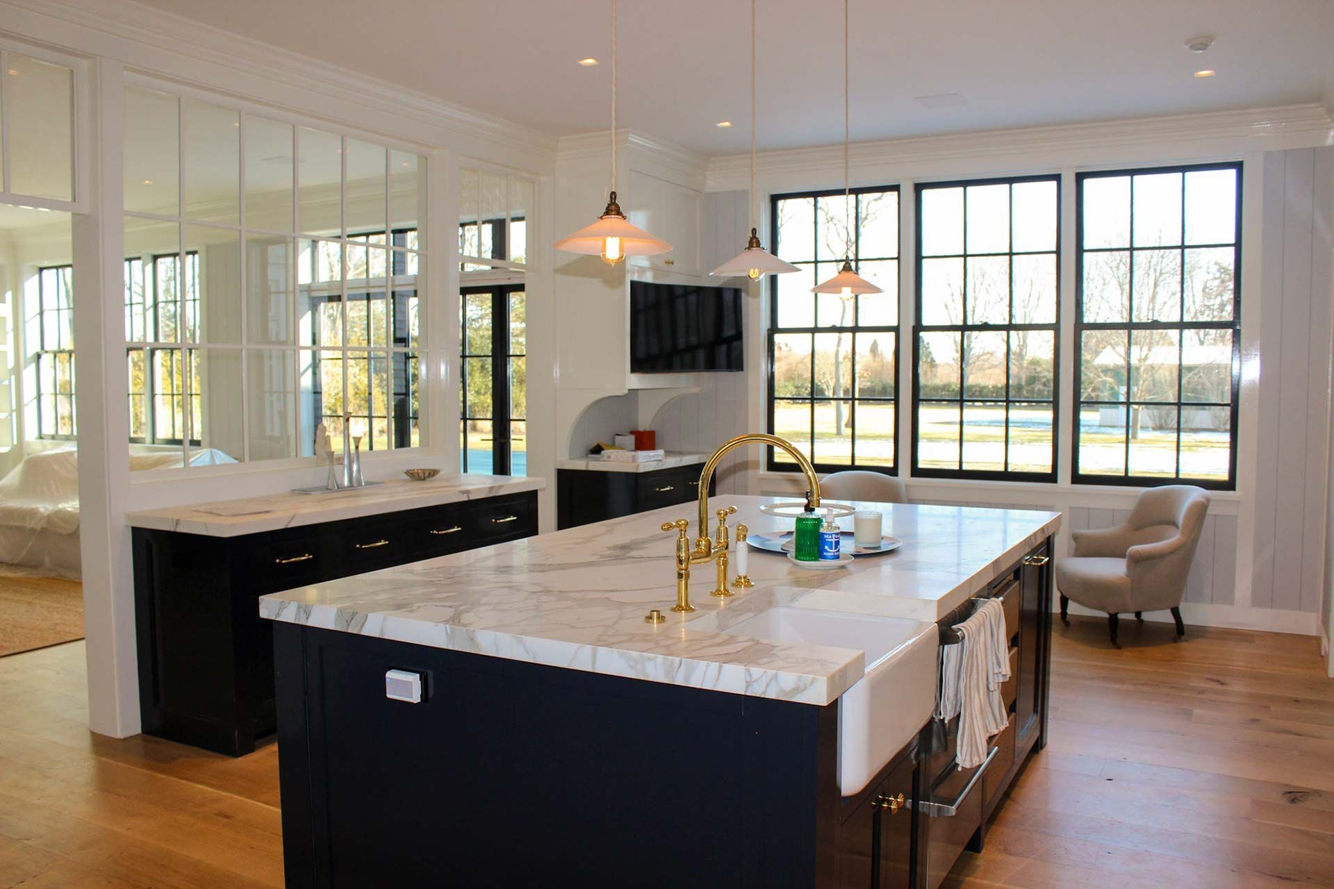 Spacious kitchen with a large island, windows, and a marble countertop, featuring a dark blue base and gold fixtures.