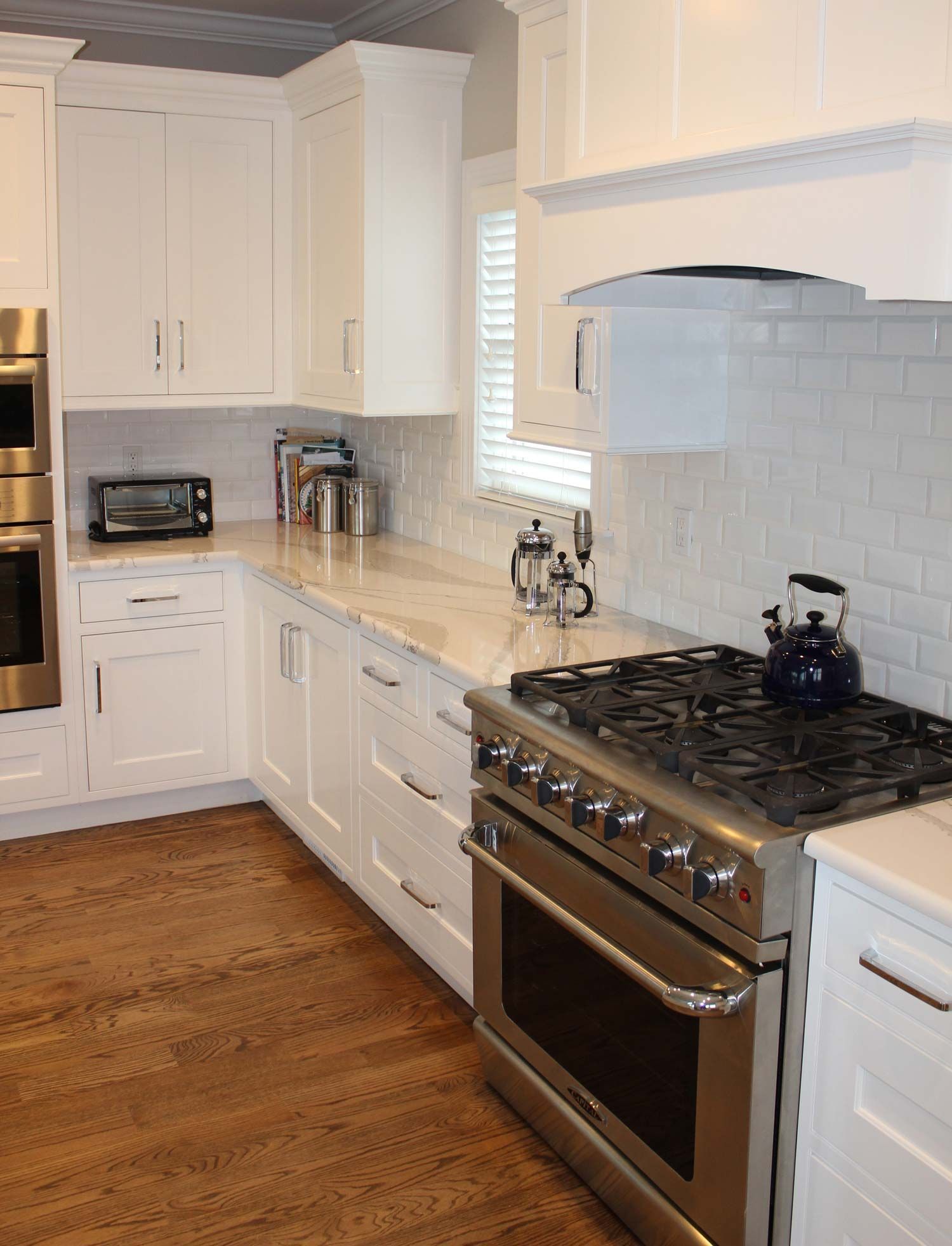 White kitchen with stainless steel appliances, light countertops, and wood flooring.