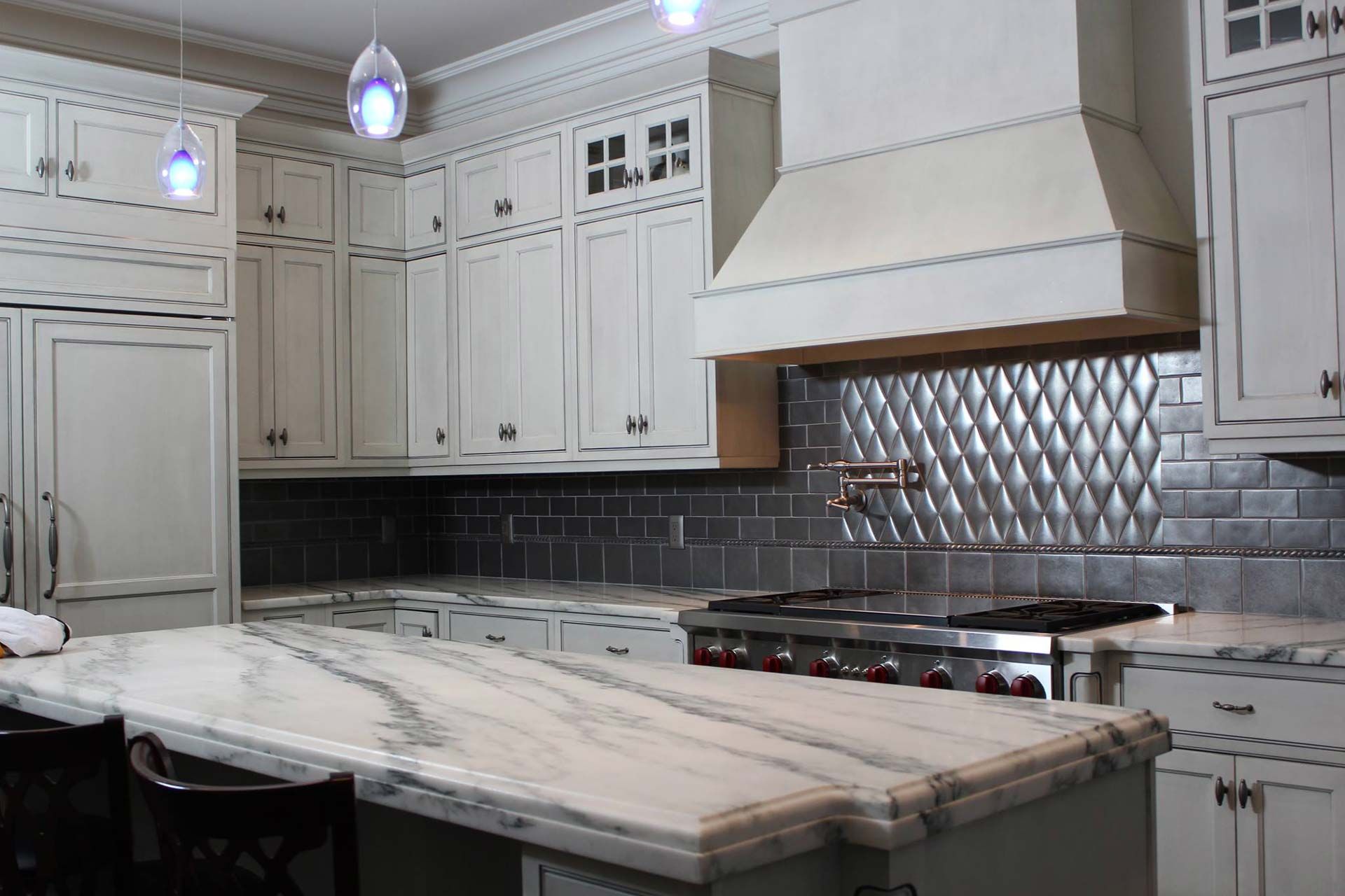White kitchen with marble island and gray tile backsplash.
