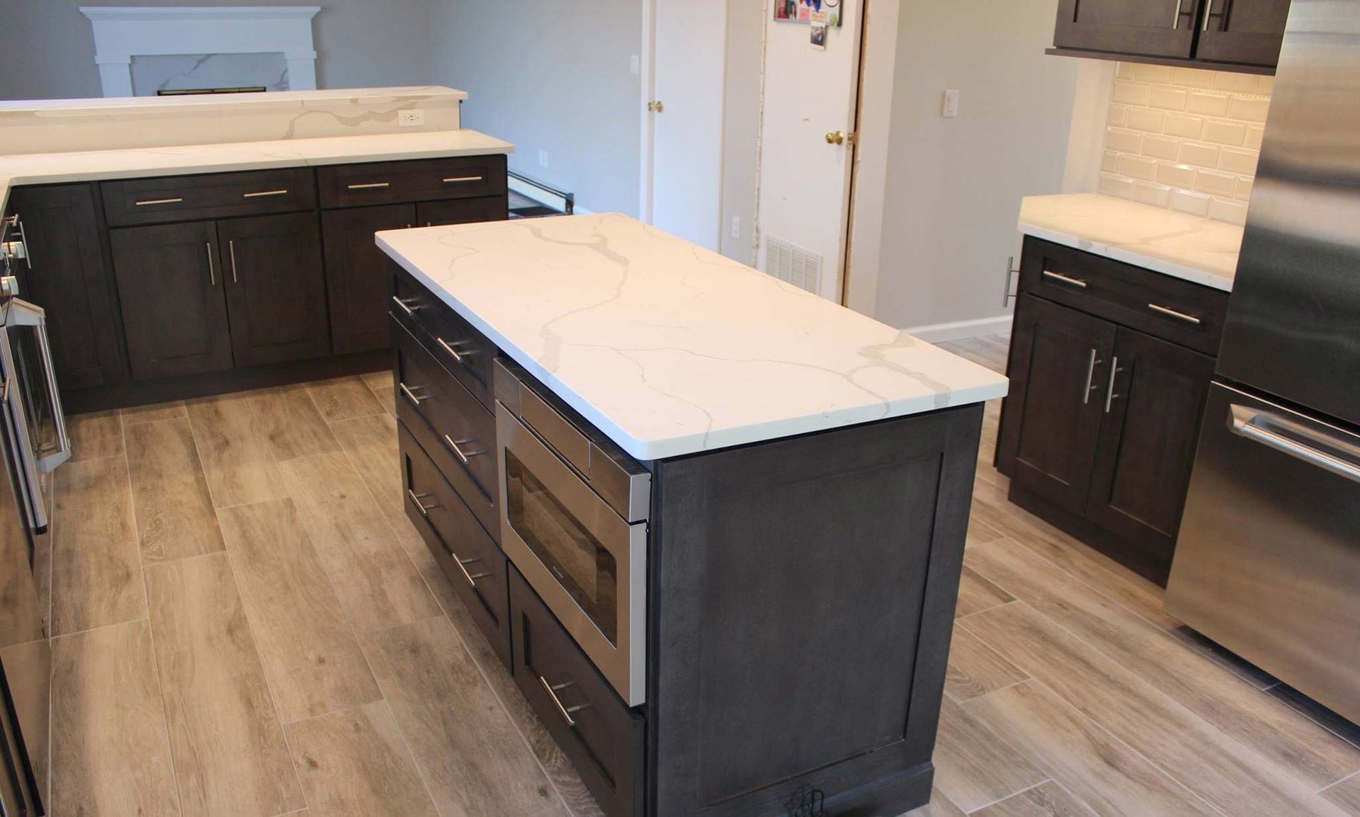 Dark cabinets and white countertops in a modern kitchen with an island and stainless steel appliances.