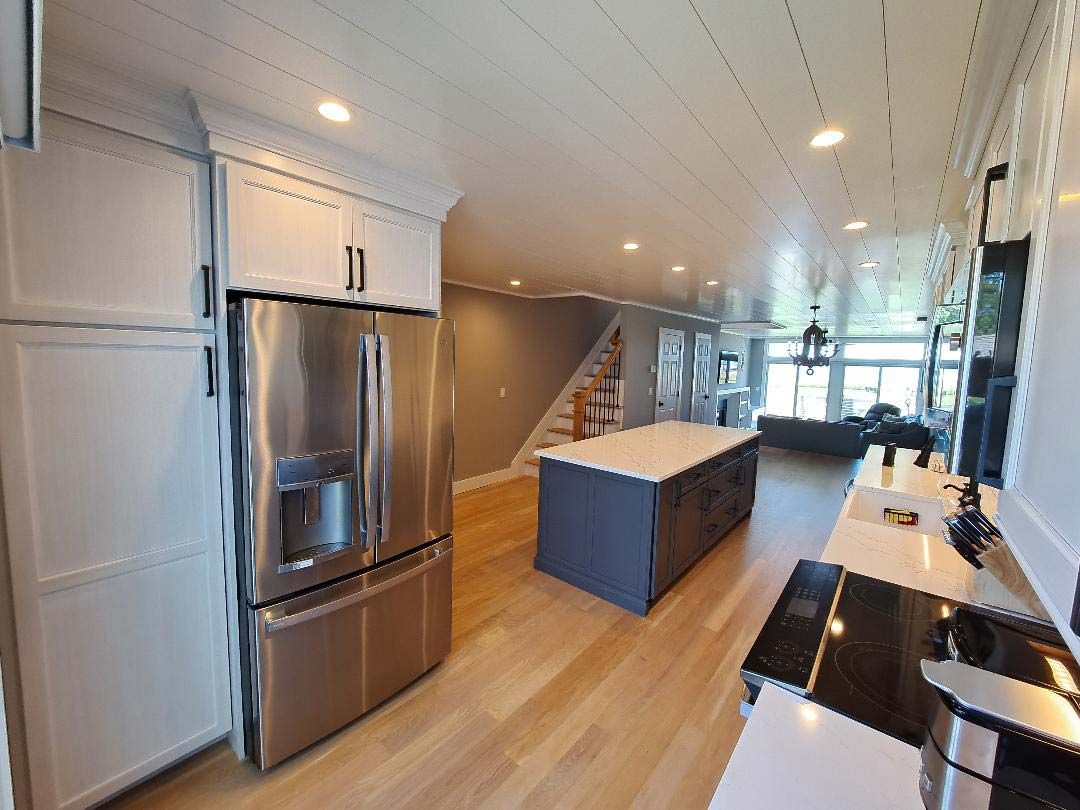 Modern kitchen with stainless steel refrigerator, island, and light wood floors.