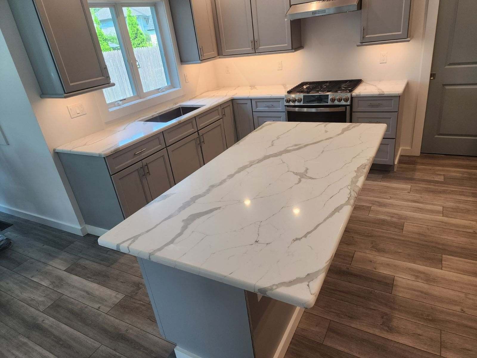 Gray kitchen with white countertops and island, gas stove, and wood-look flooring.