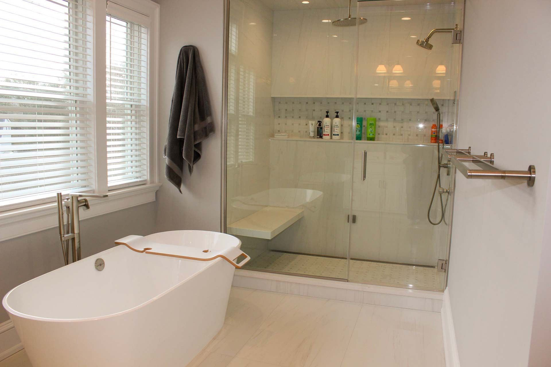 Bathroom with a white bathtub, glass shower, and a window with blinds.