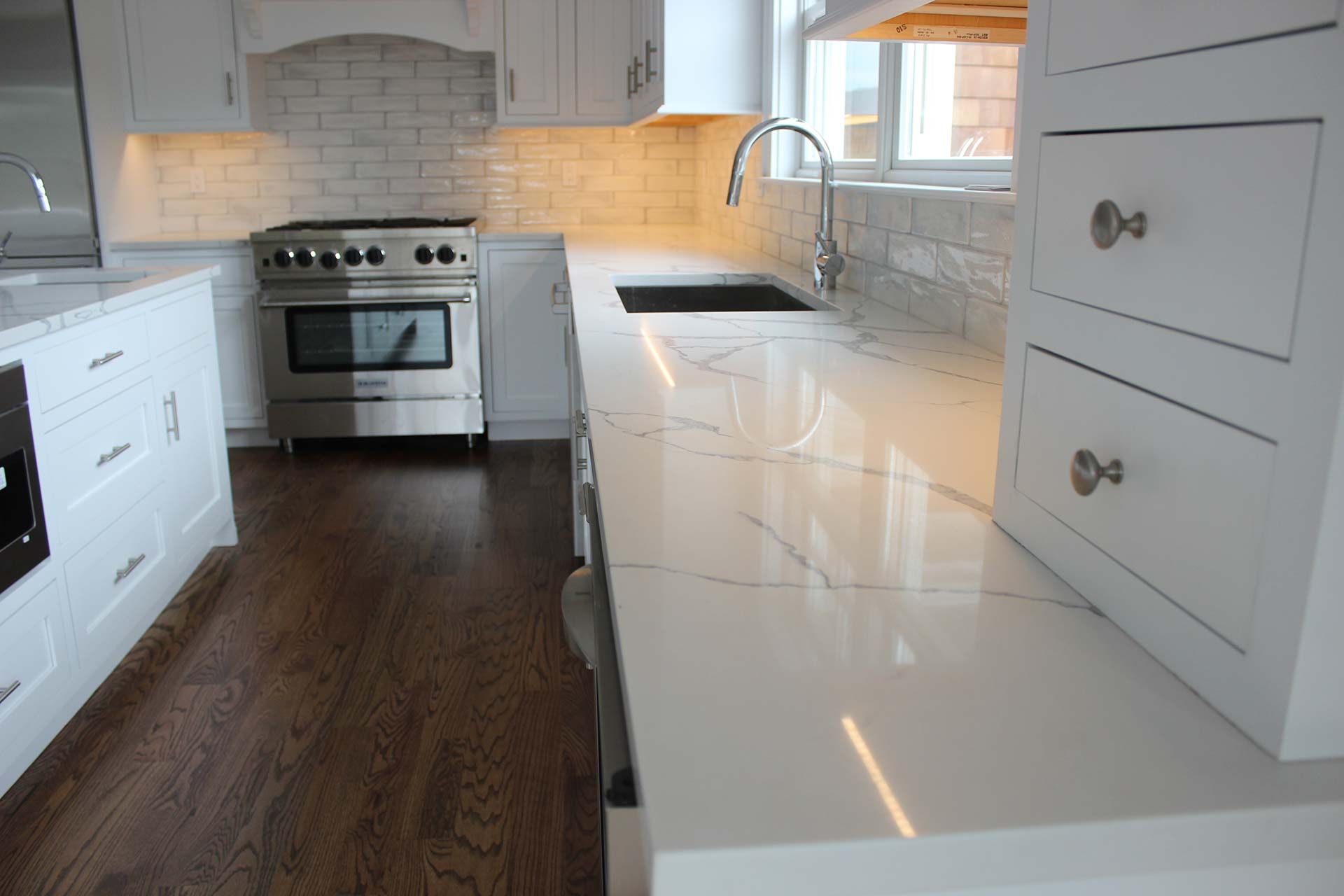White kitchen with marble countertops, stainless steel range, and dark wood floors.