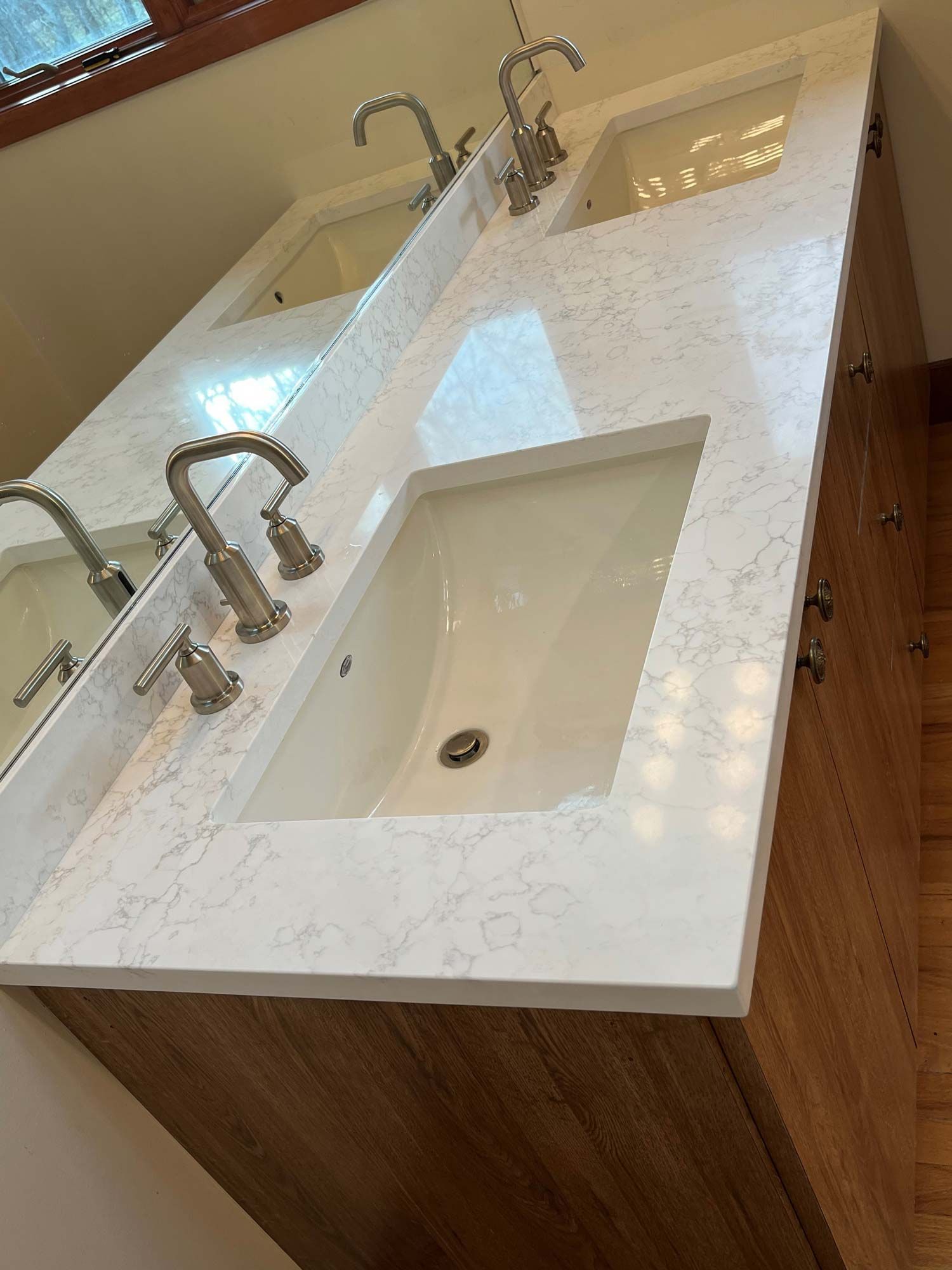 Bathroom vanity with two sinks, light countertop, wood cabinet, and brushed nickel faucets.