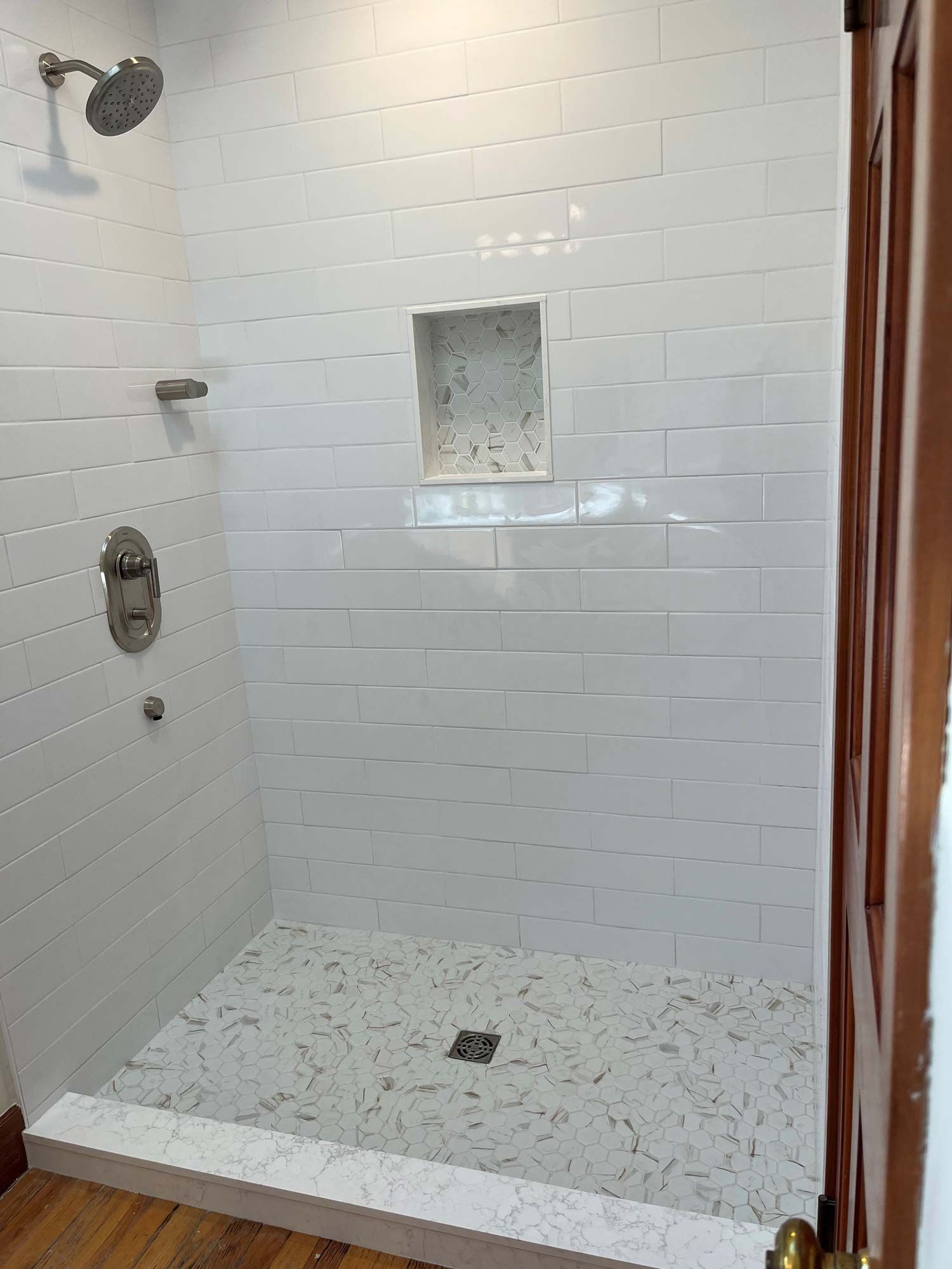 White-tiled shower with a pebble-stone floor and built-in shelf, accessed through a wooden door.