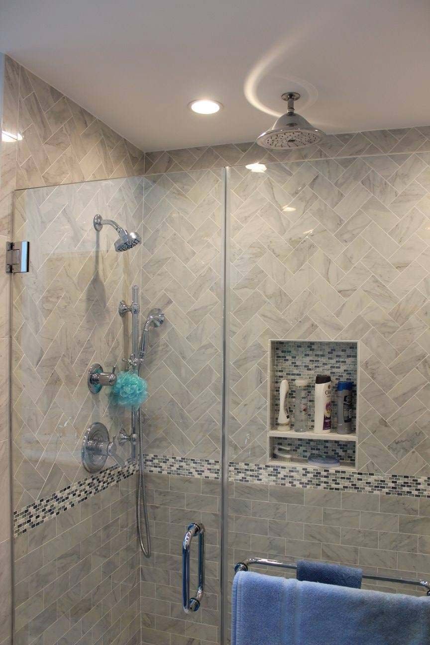 Shower with glass door, tiled walls, built-in shelf. Silver fixtures, light gray, blue accents.