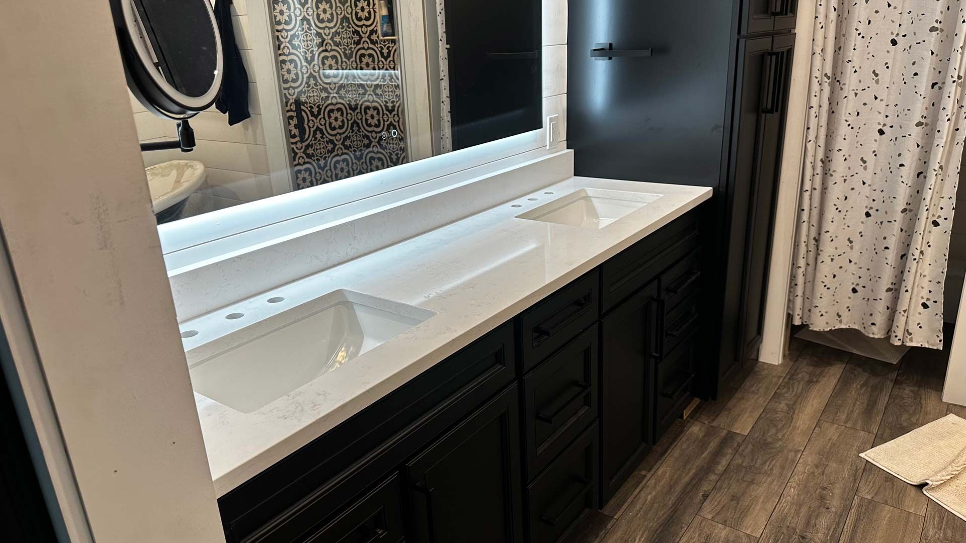 Black double vanity with white countertop and sinks. Bathroom with a mirror, shower curtain, and wood-look floor.