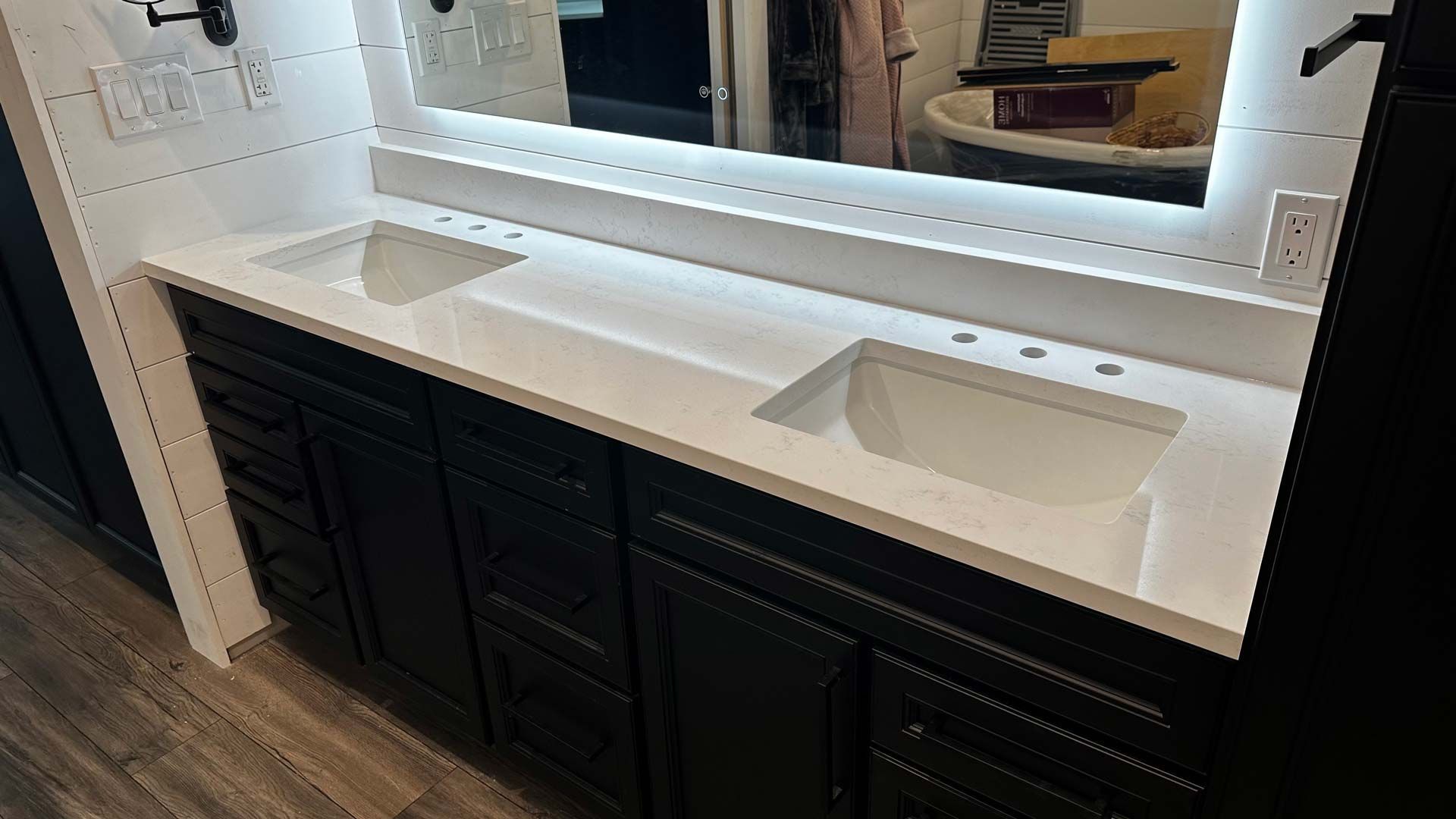 Black double vanity with white countertop and sinks; lit mirror.