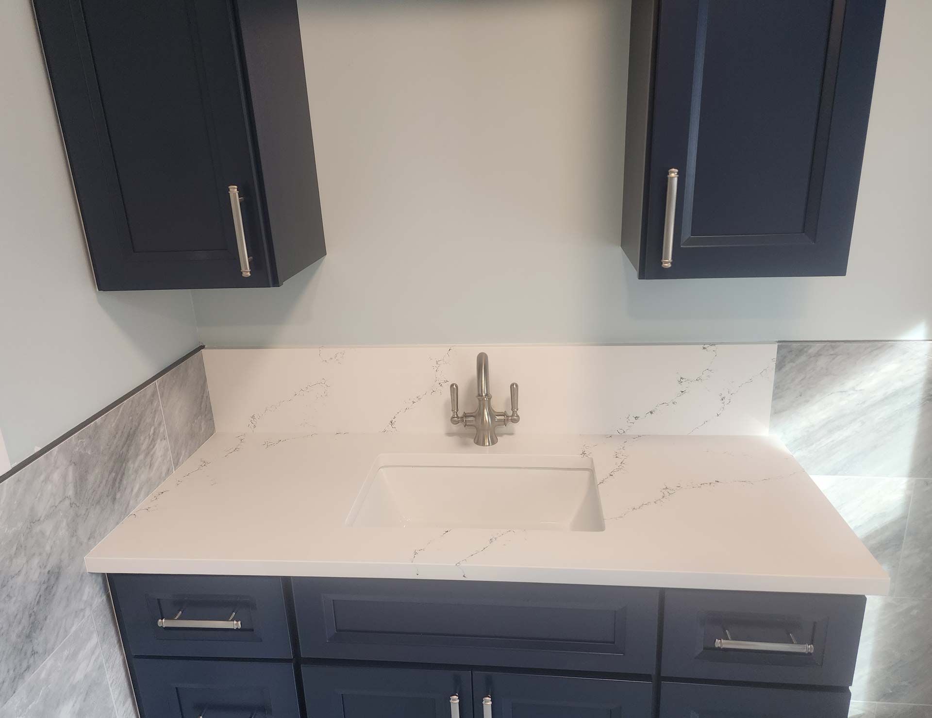 Bathroom vanity with a navy blue cabinet, white countertop, and two wall cabinets.