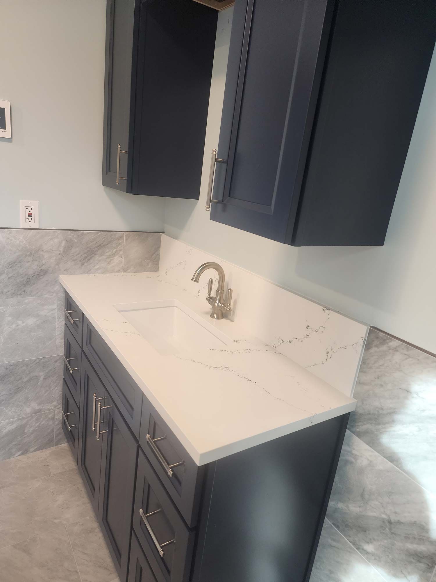 Navy blue vanity with a white countertop and gold faucet under matching cabinets against a tiled wall.