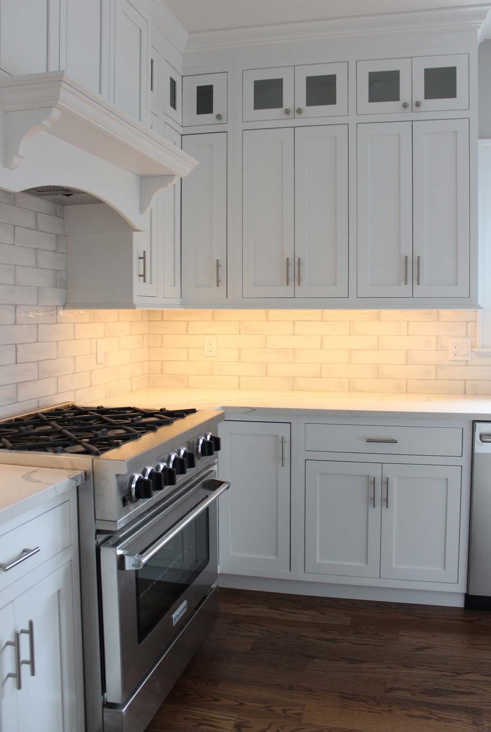 White kitchen with stainless steel appliances, cabinets, and wood floors.