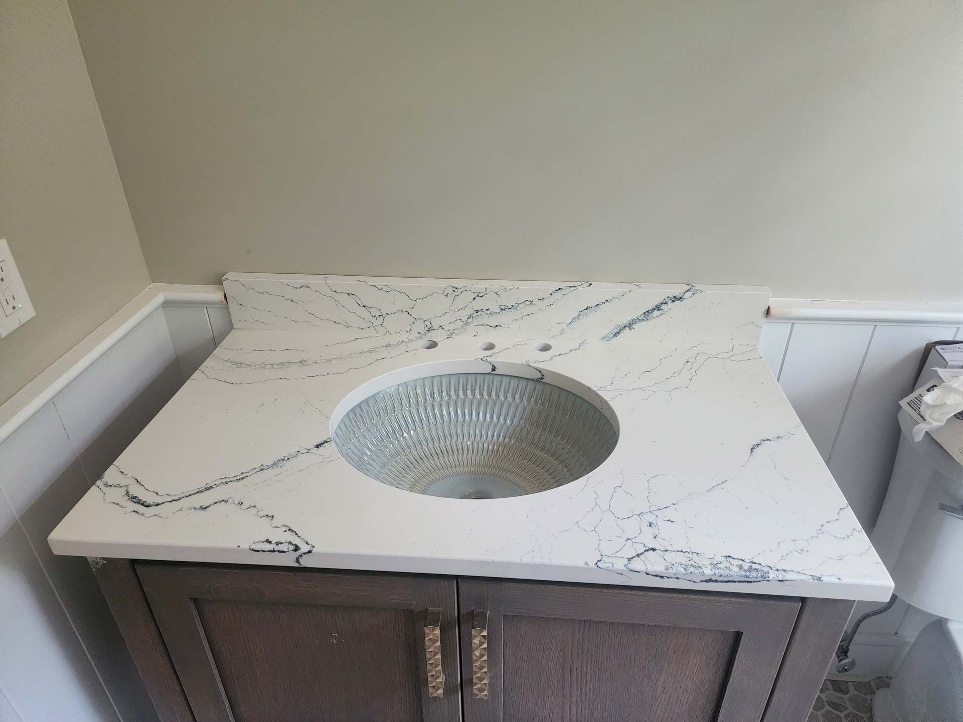 Vanity with white countertop, black veining, and round sink. Dark wood cabinet.