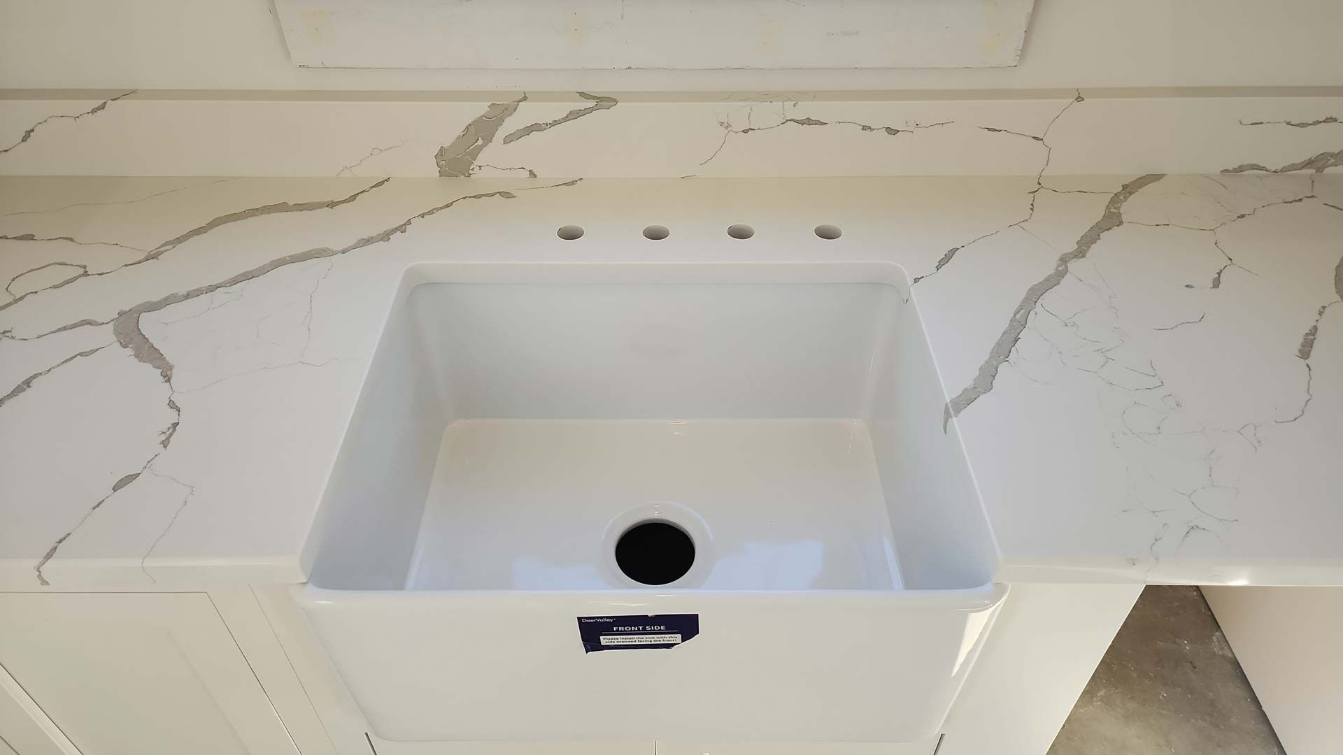 White rectangular sink in a white countertop with grey veining, four faucet holes.