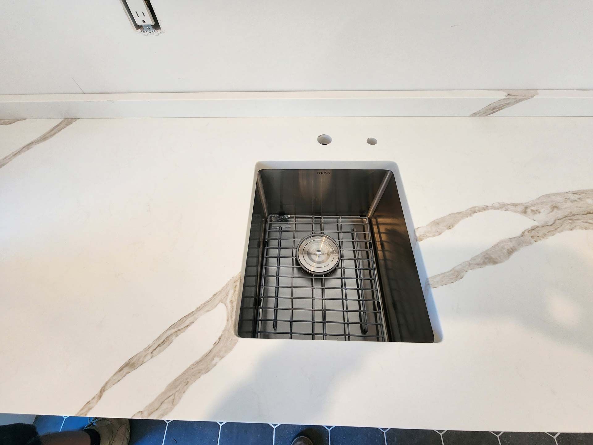 Stainless steel kitchen sink in white quartz countertop with beige veining.