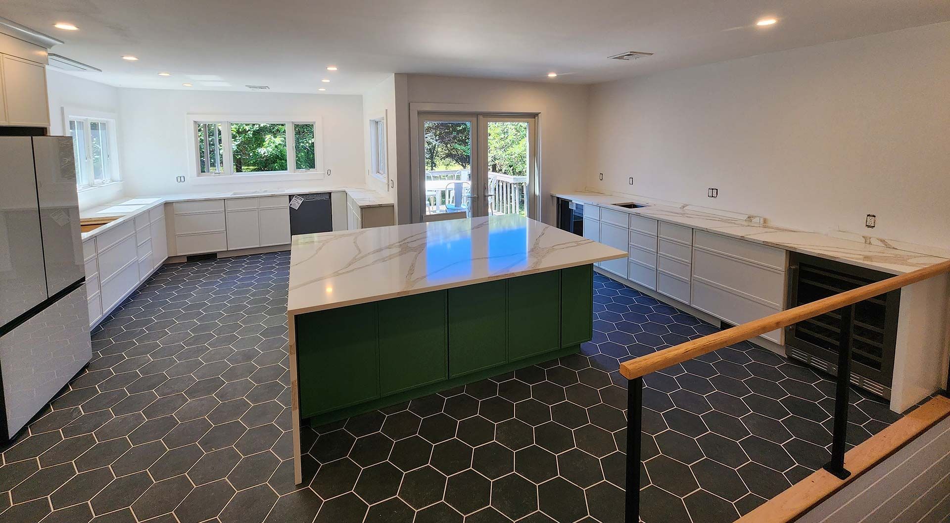 Kitchen with green island, white cabinets, black hexagon floor tiles, and access to a deck.