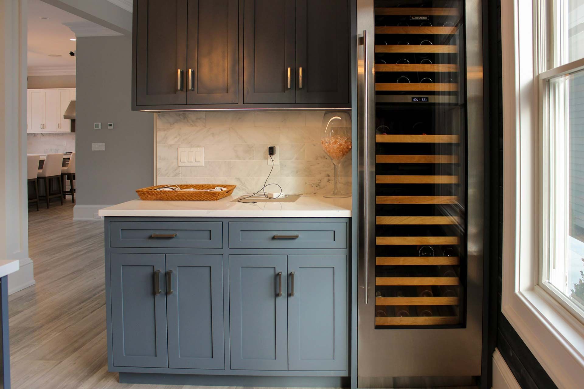 Dark blue cabinets with a wine fridge, marble countertop, and off-white tile backsplash.