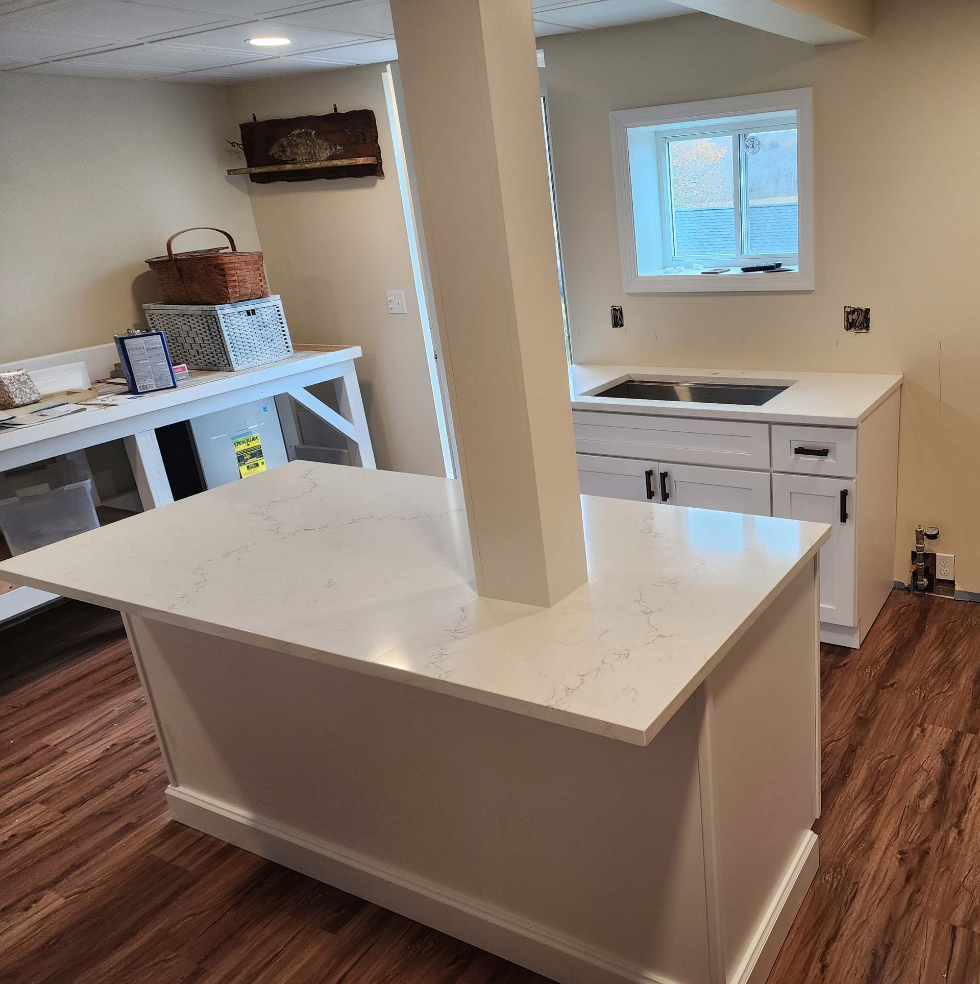 White kitchen with island, sink, counters, and structural column in a finished basement.