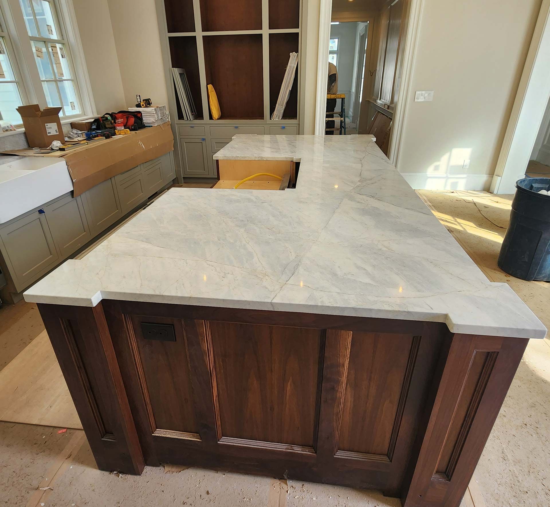 A kitchen island with a marble countertop and dark wood cabinets is in a room under construction.
