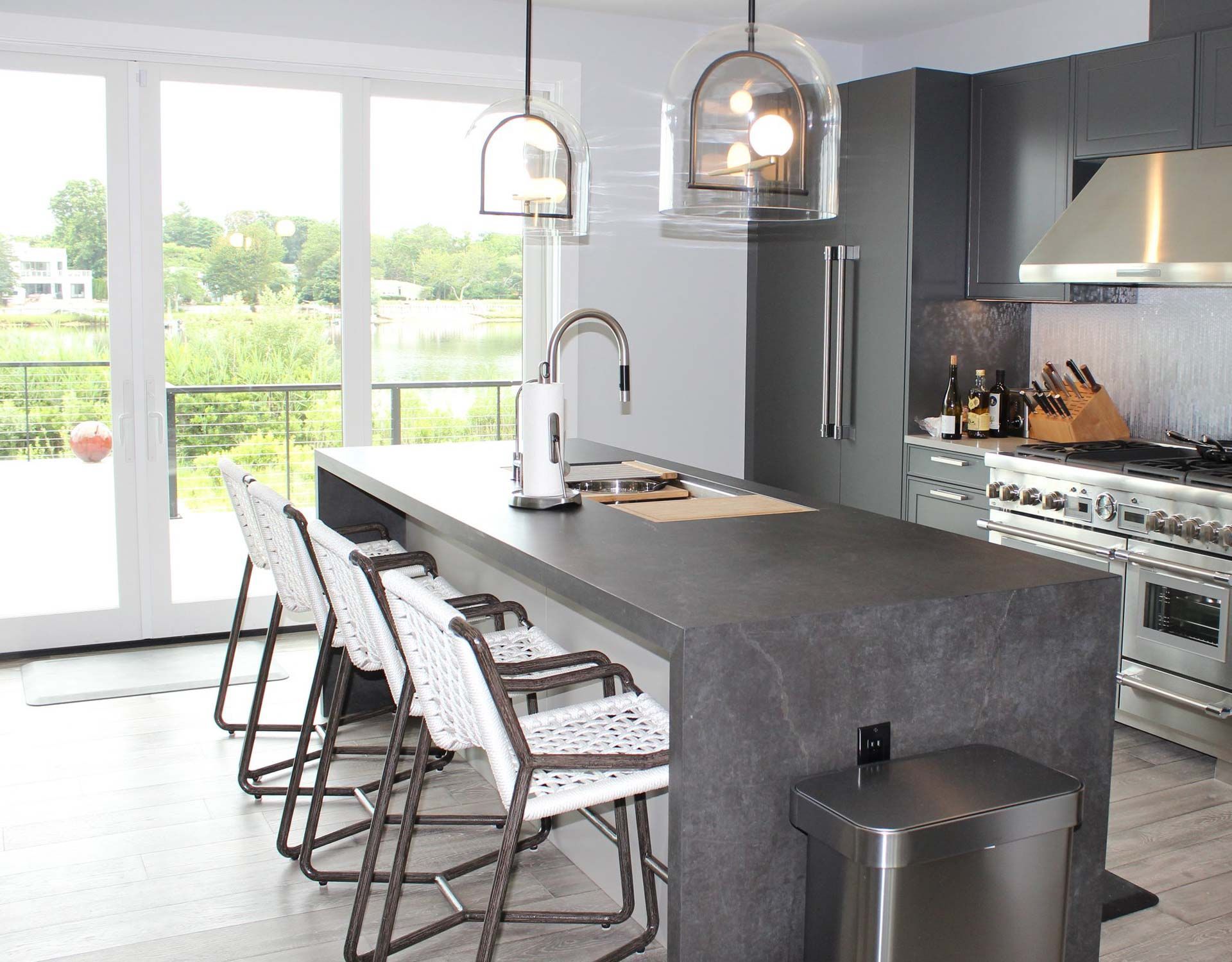 Modern kitchen with gray cabinets, island with seating, and a view of water and trees.