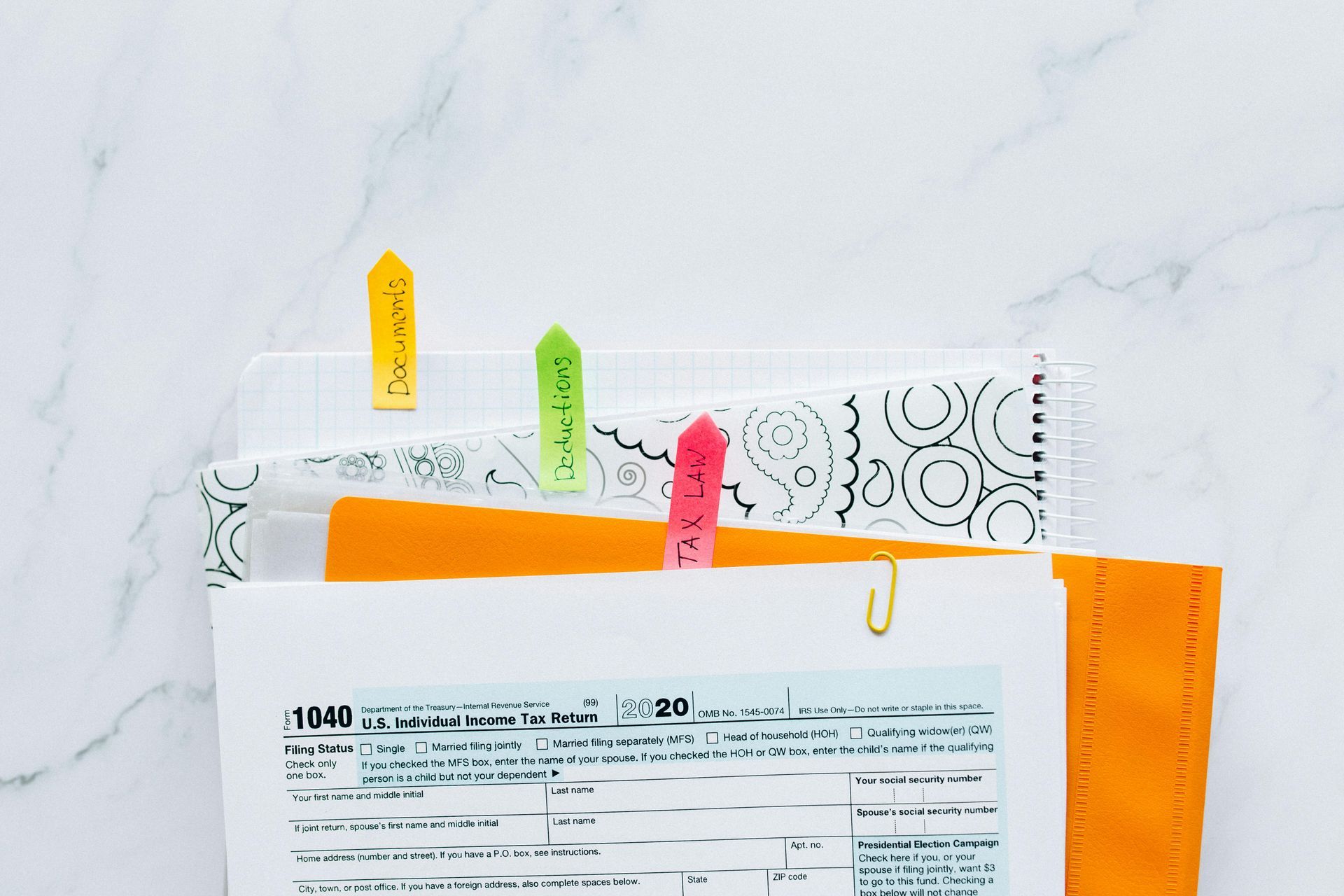 Tax documents clipped together with colorful sticky notes, gold paper clip, on marble surface.